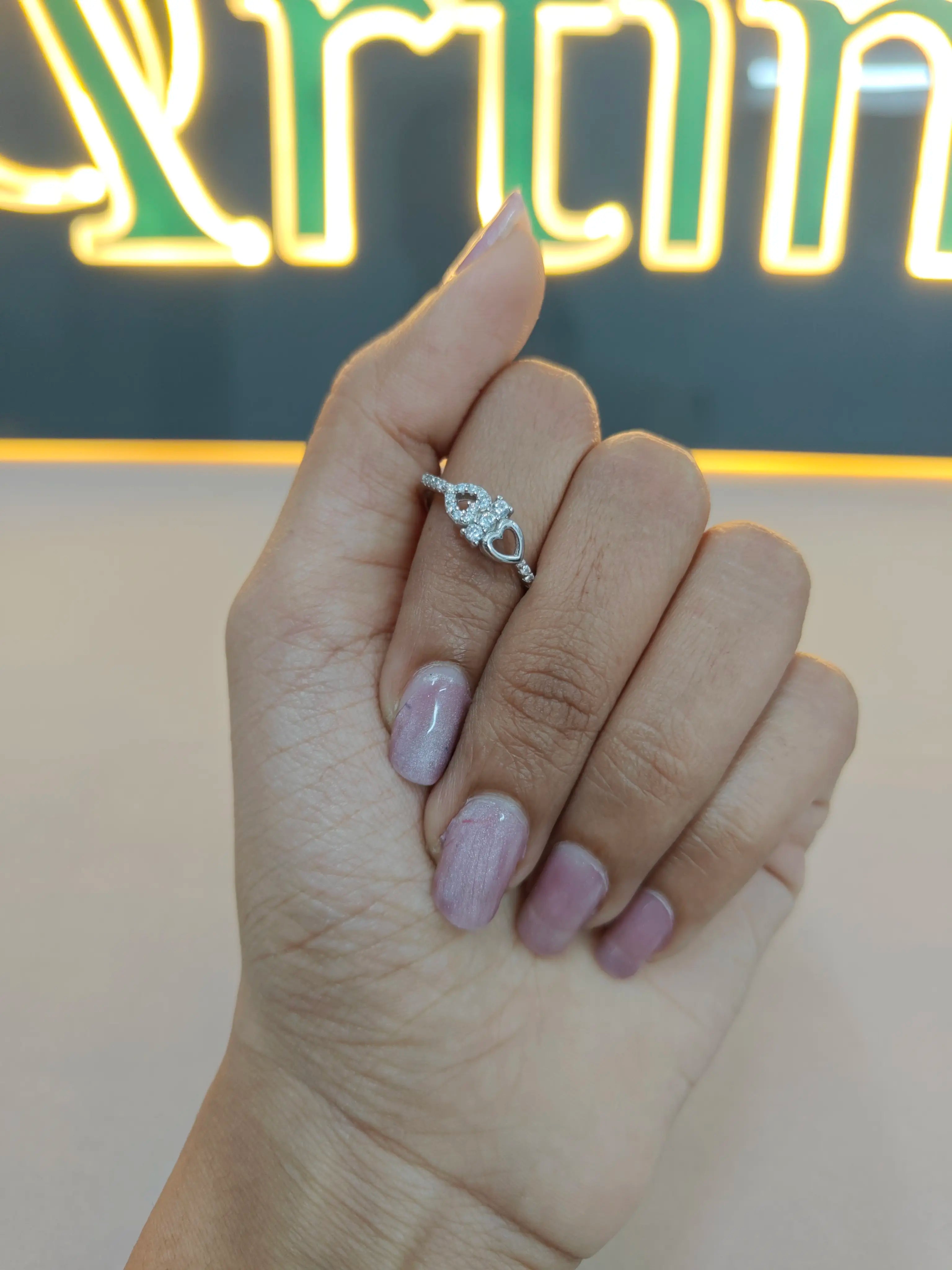 Hand wearing a silver ring with a blurred neon sign in the background