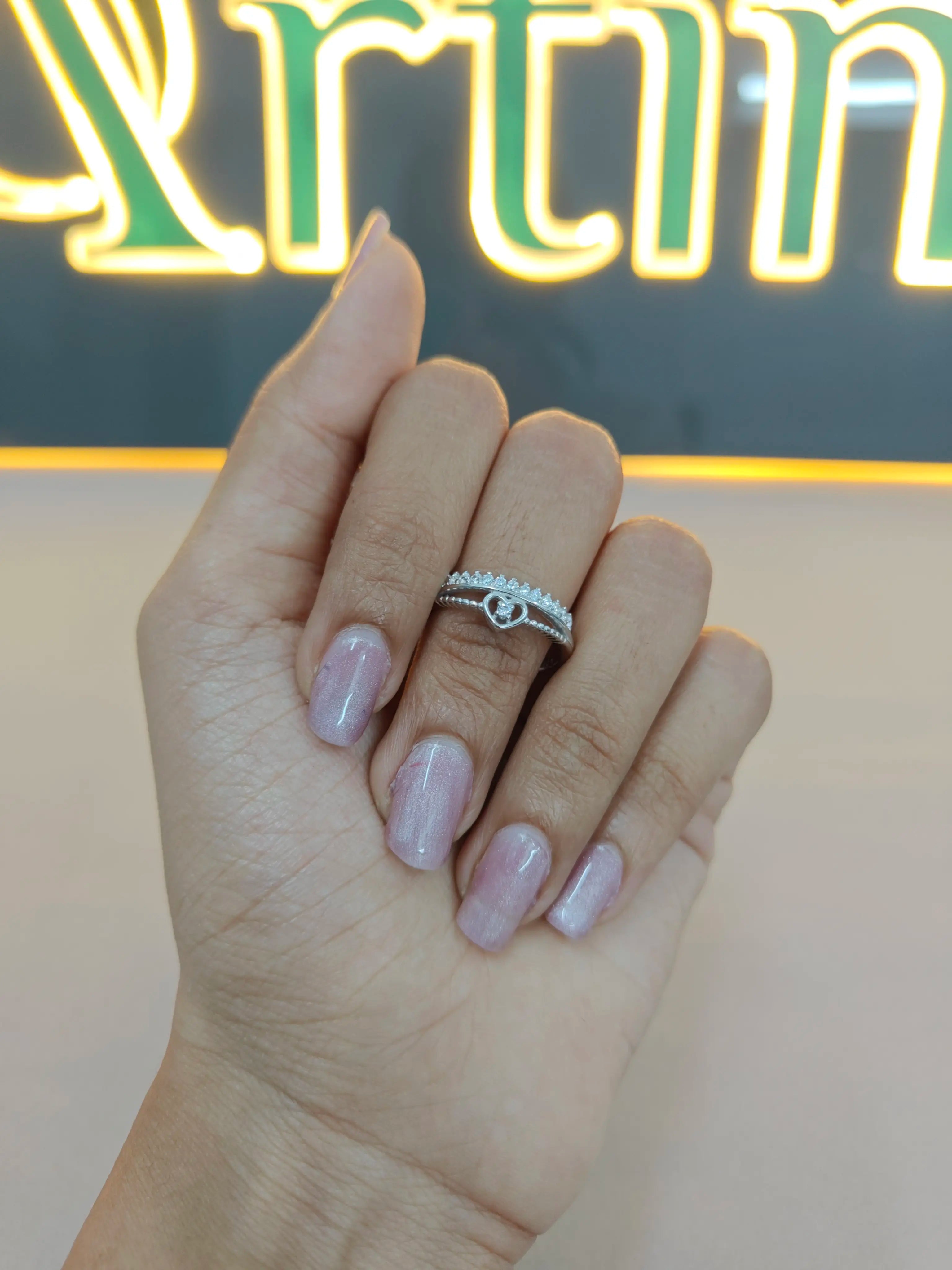 Hand wearing a silver ring with a visible brand logo in the background