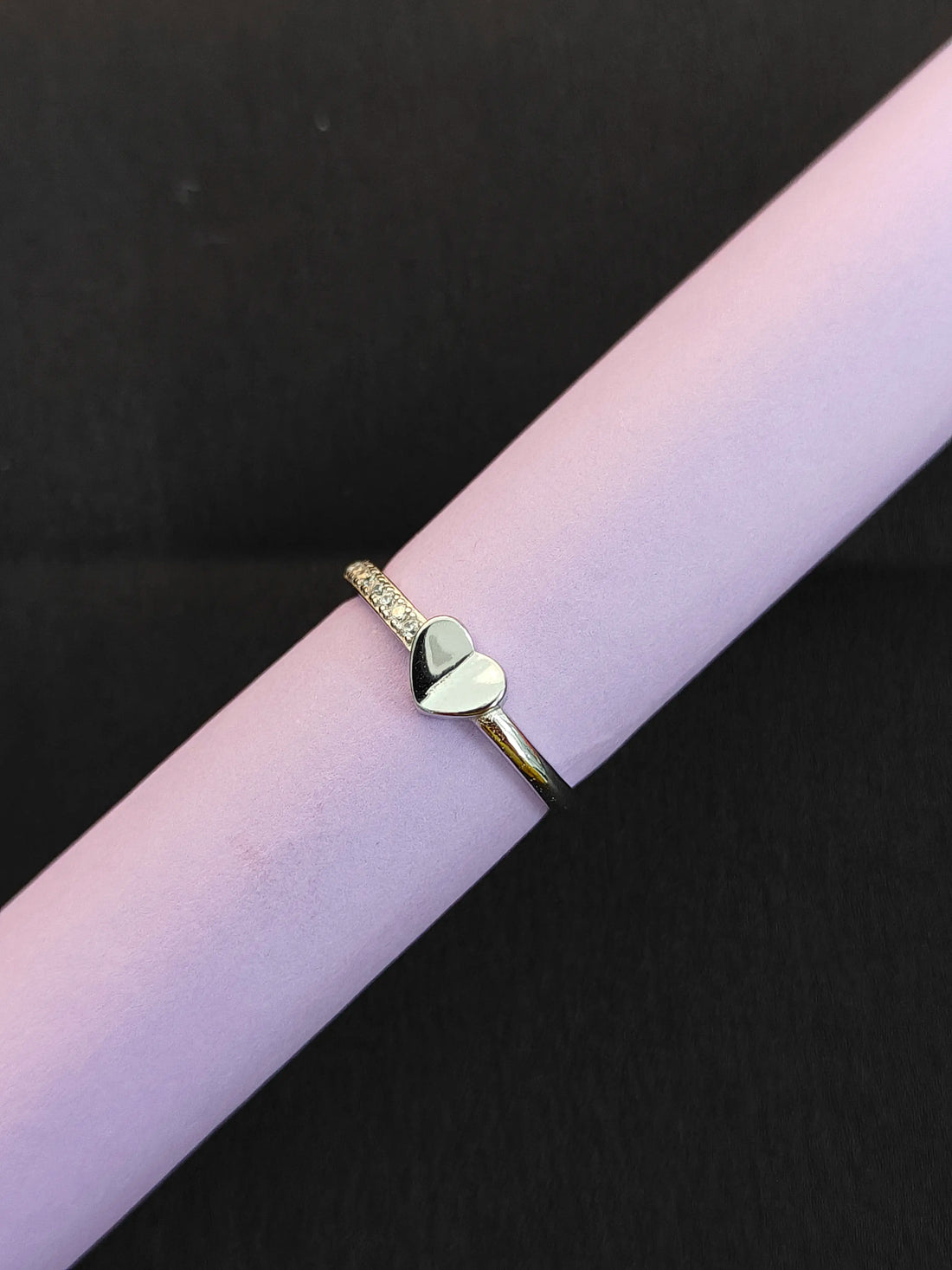 Gold ring with a heart-shaped charm on a pink surface
