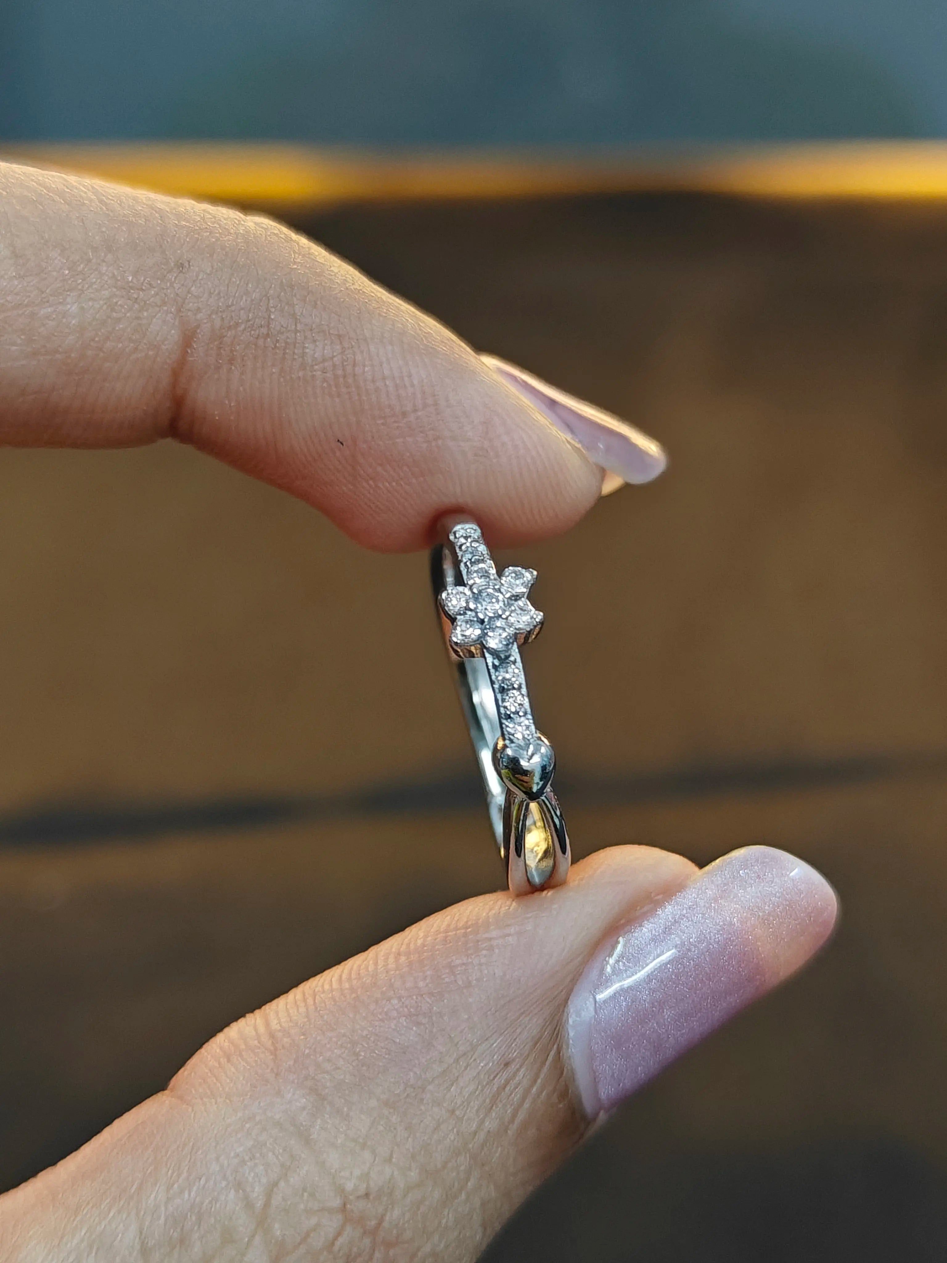 Silver ring with a floral design held between fingers against a blurred background