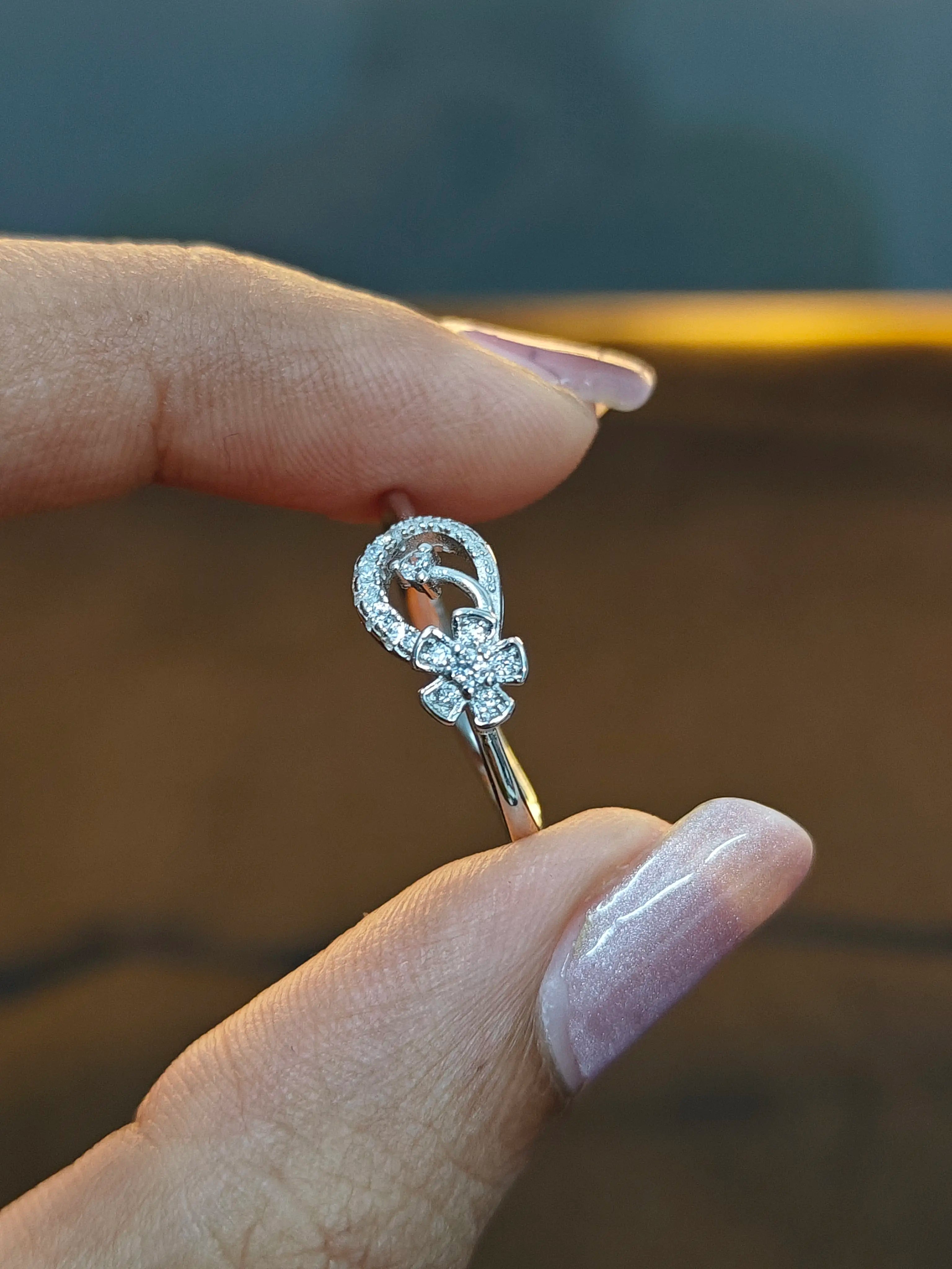 Silver ring with intricate design held between fingers against a blurred background