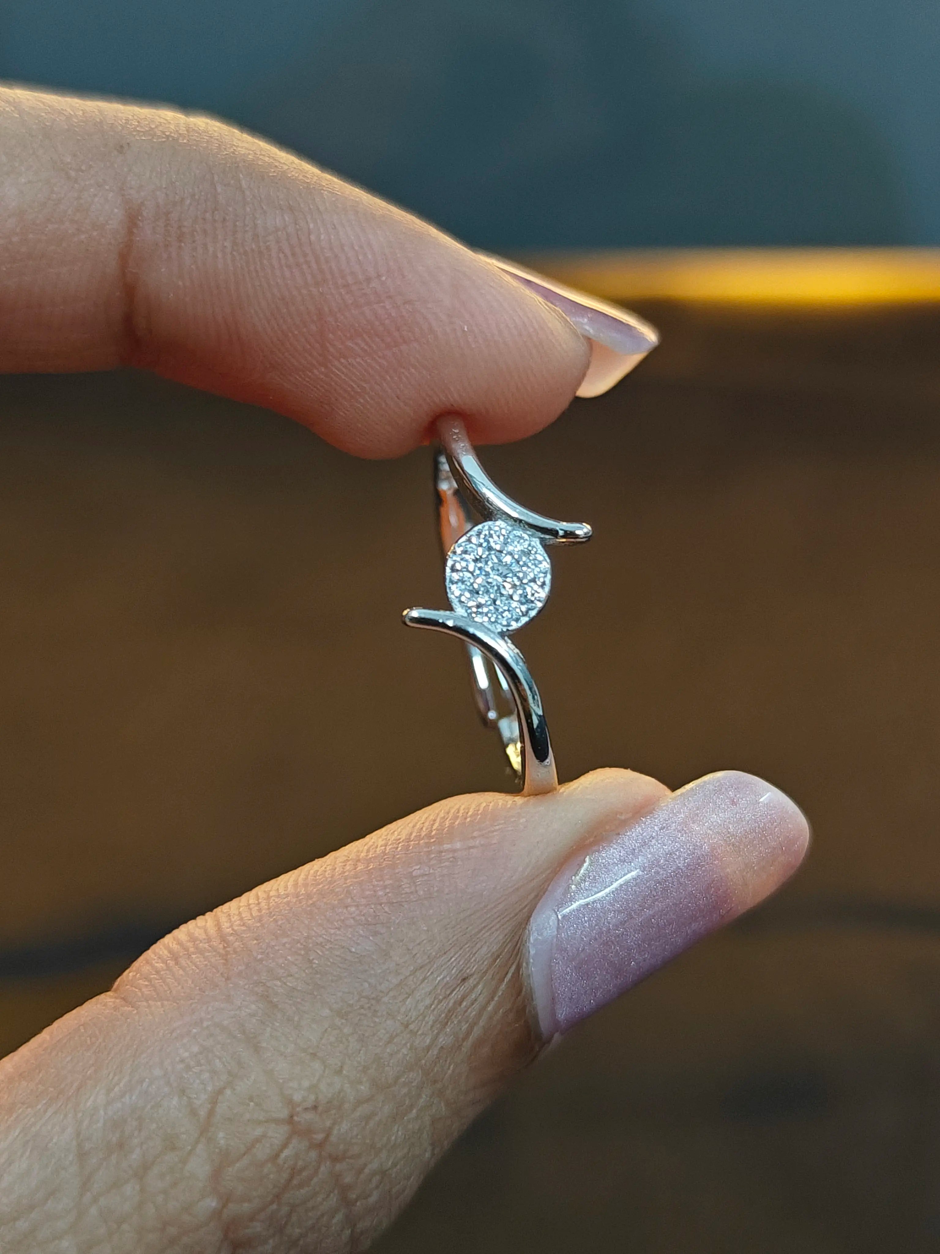 Silver earring with a diamond held between fingers against a blurred background