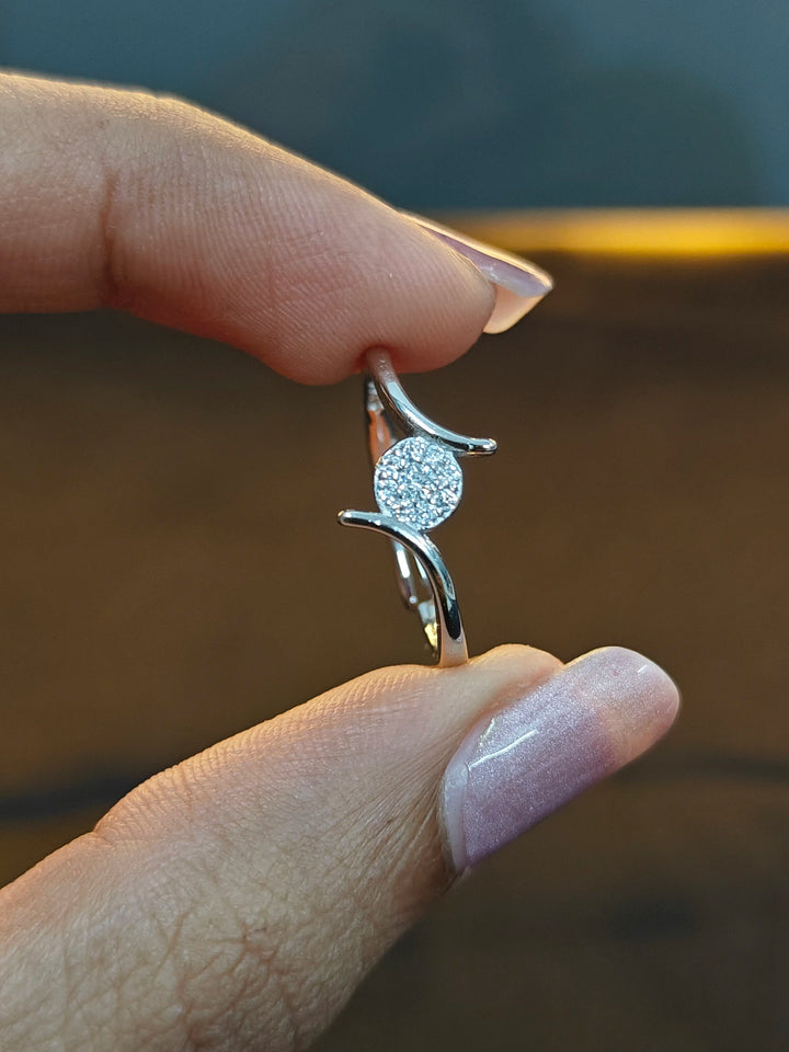Silver earring with a diamond held between fingers against a blurred background