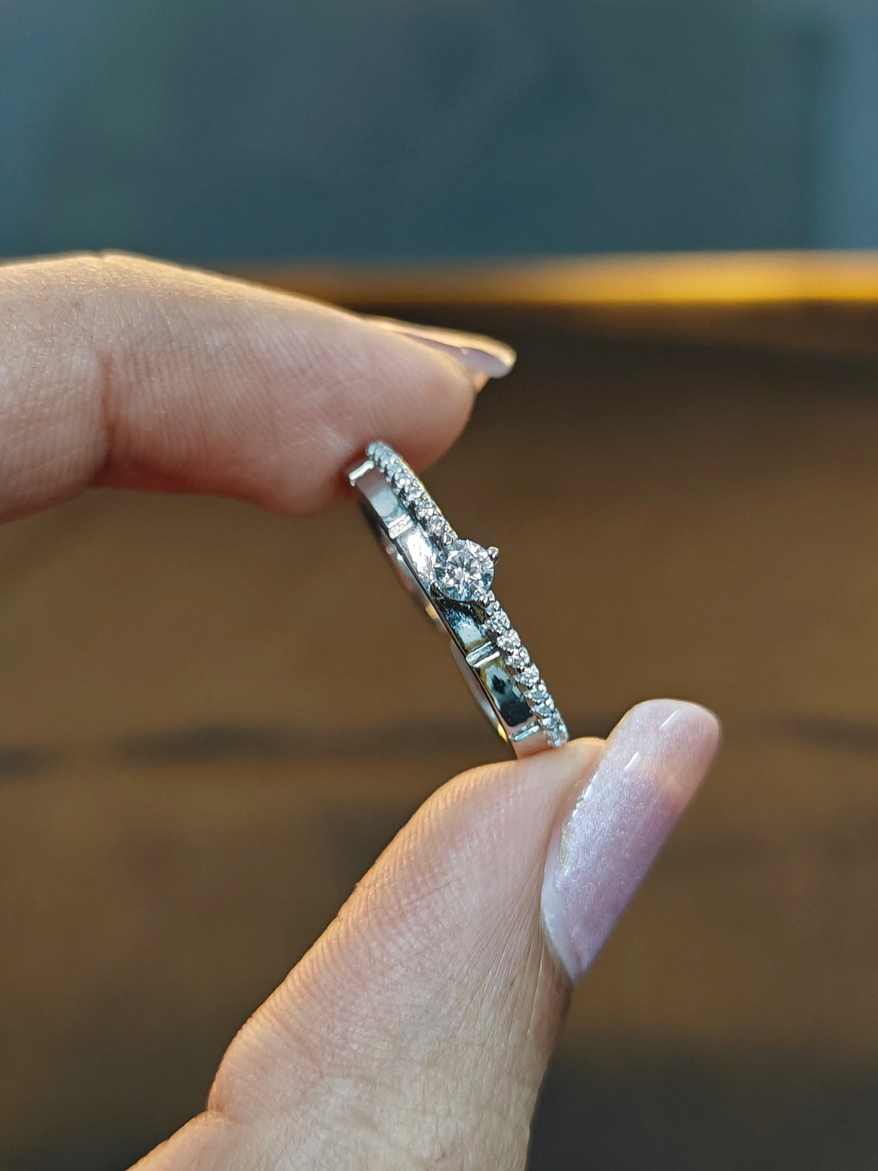 Silver ring with gemstones held between fingers against a blurred background