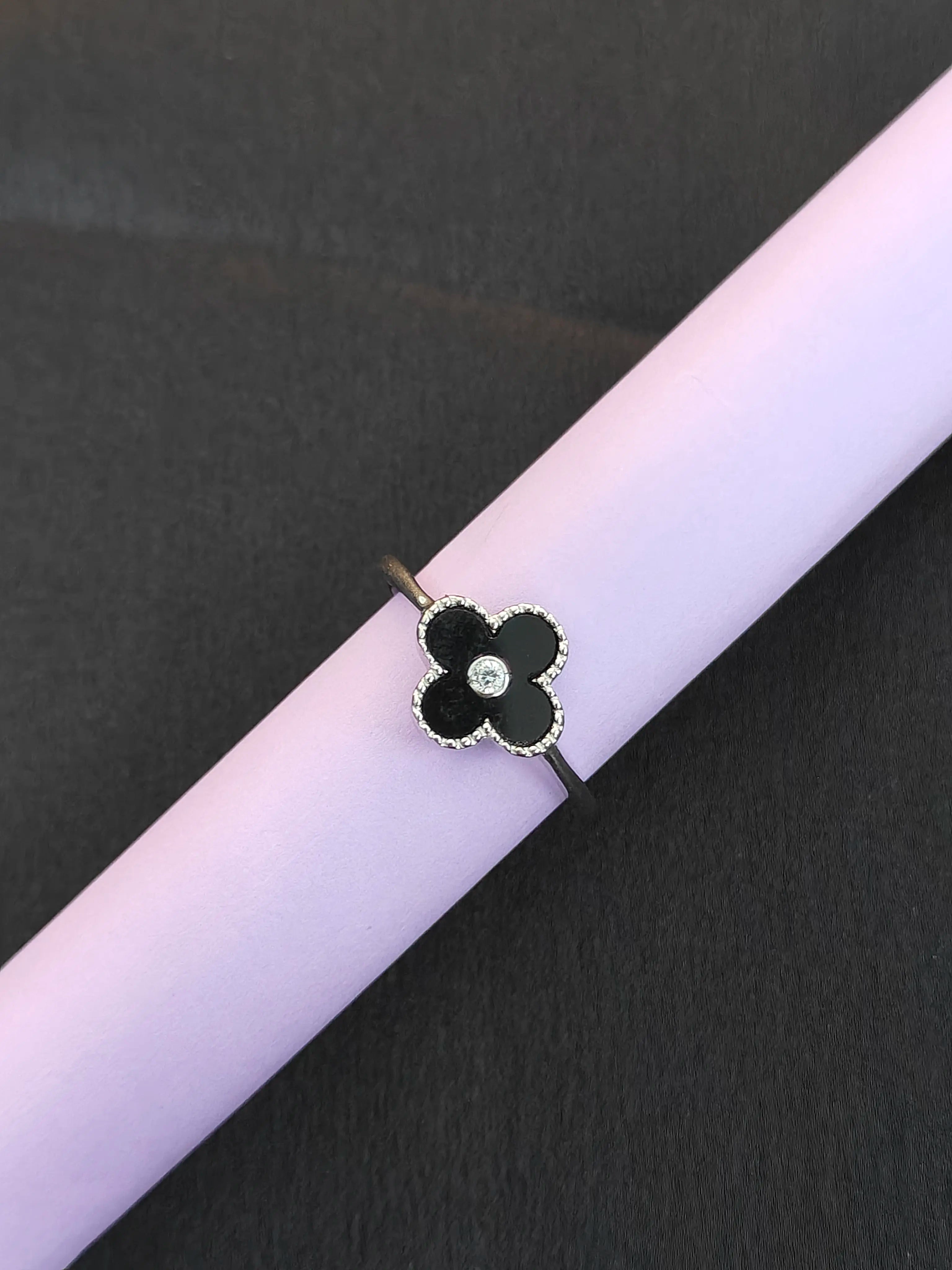 Black flower-shaped ring with a diamond on a pink surface