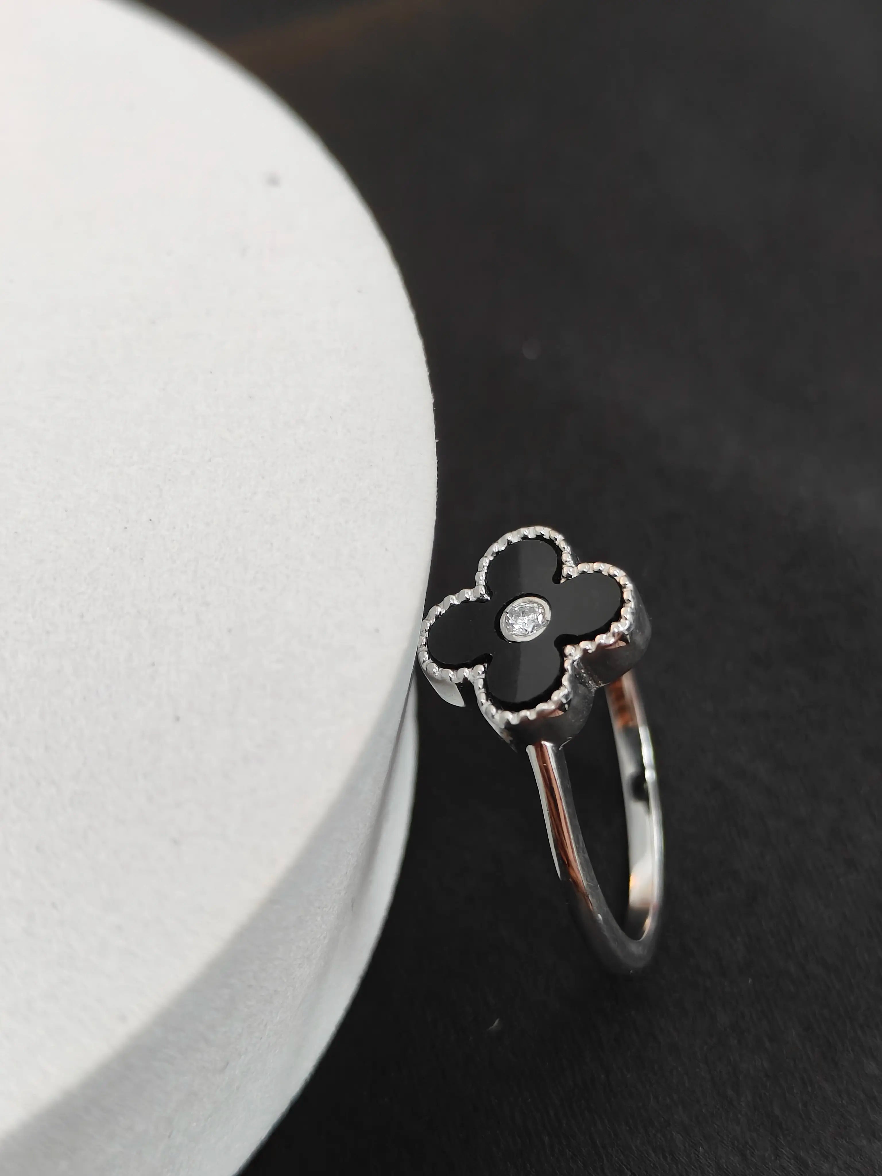 Silver ring with black clover-shaped setting on a dark surface