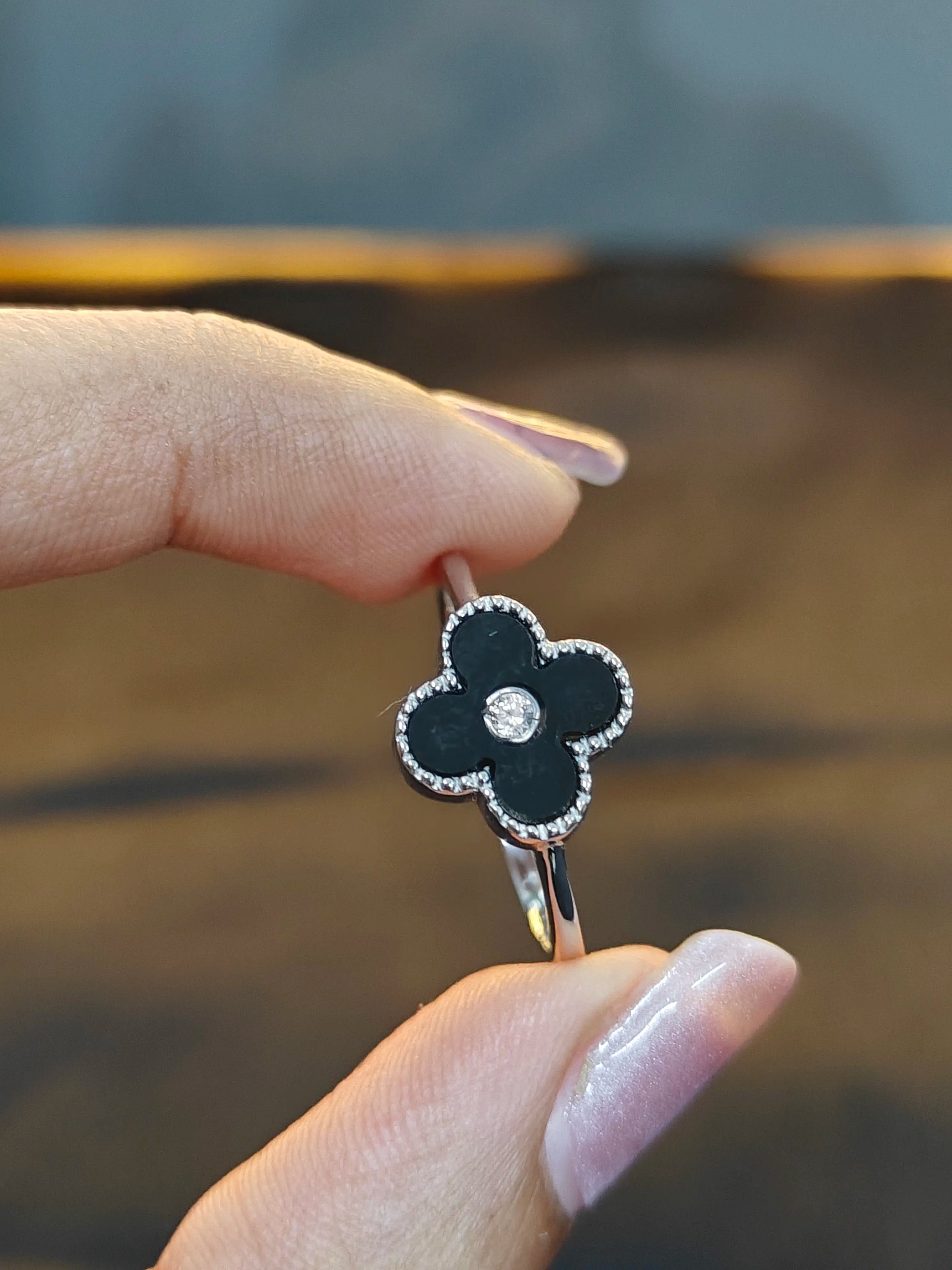 Black clover-shaped ring with a silver band held by a hand against a blurred background