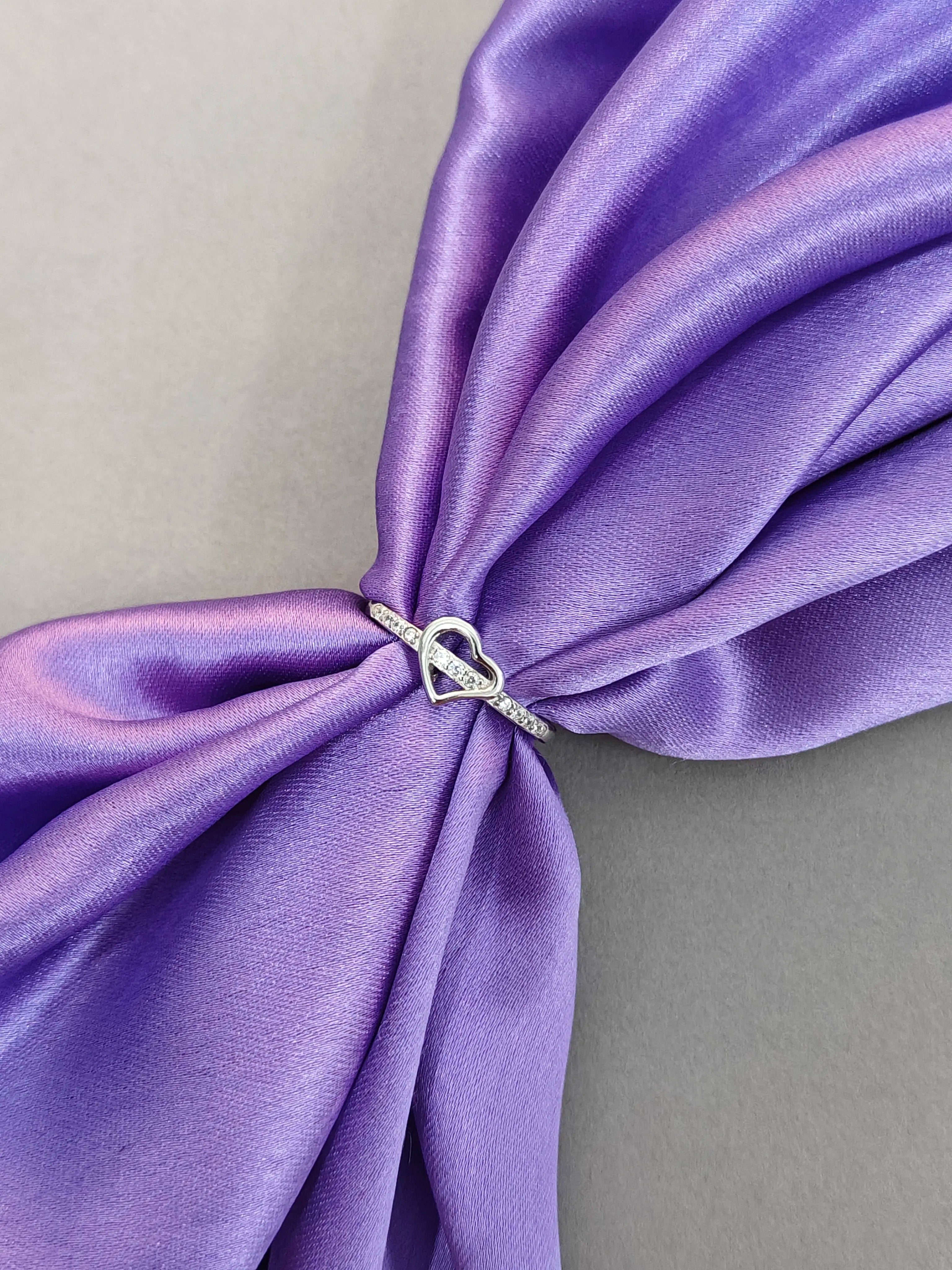 Silver ring with a heart design on a purple fabric background