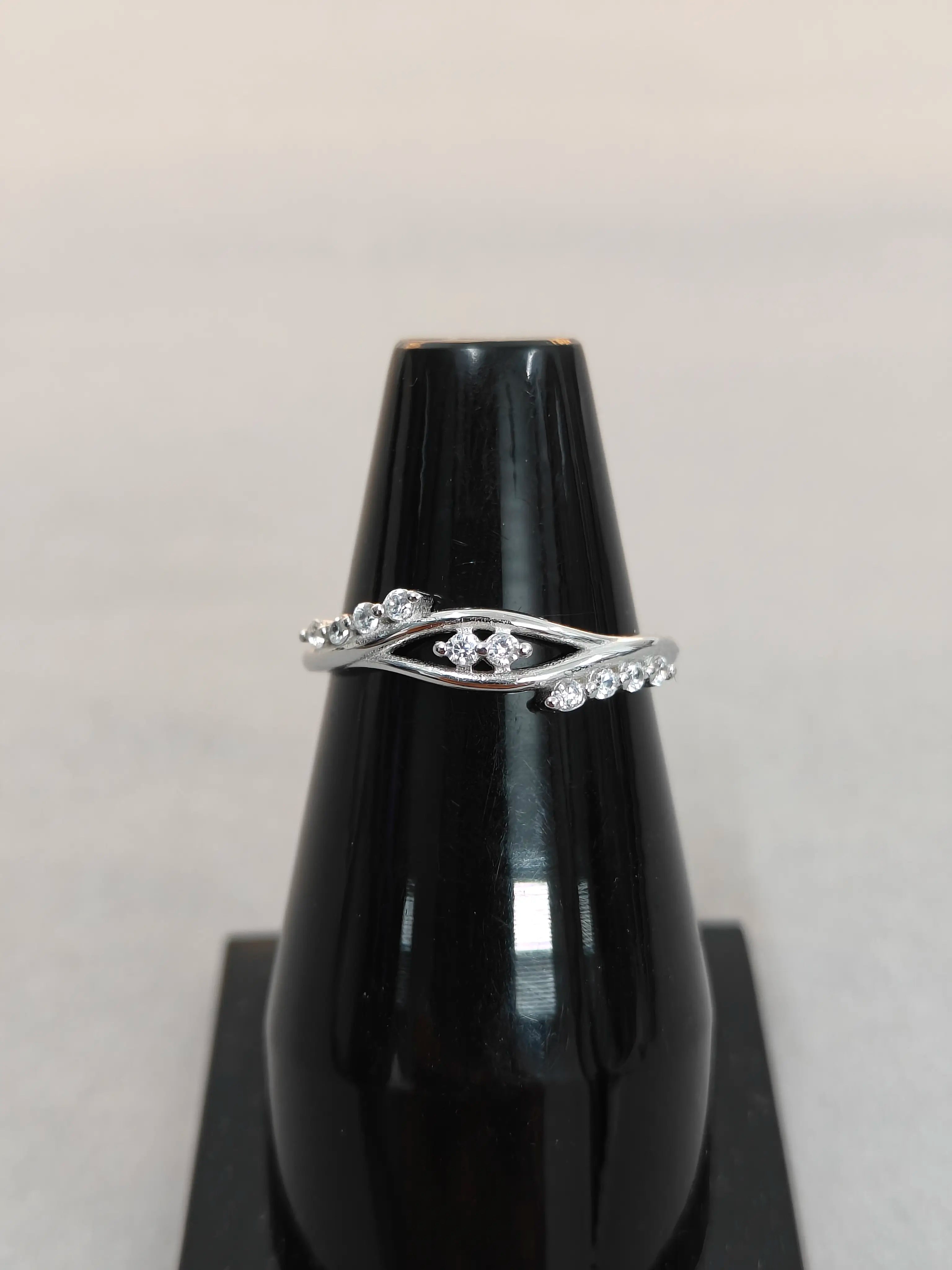 Silver ring with gemstones on a black vase against a light gray background