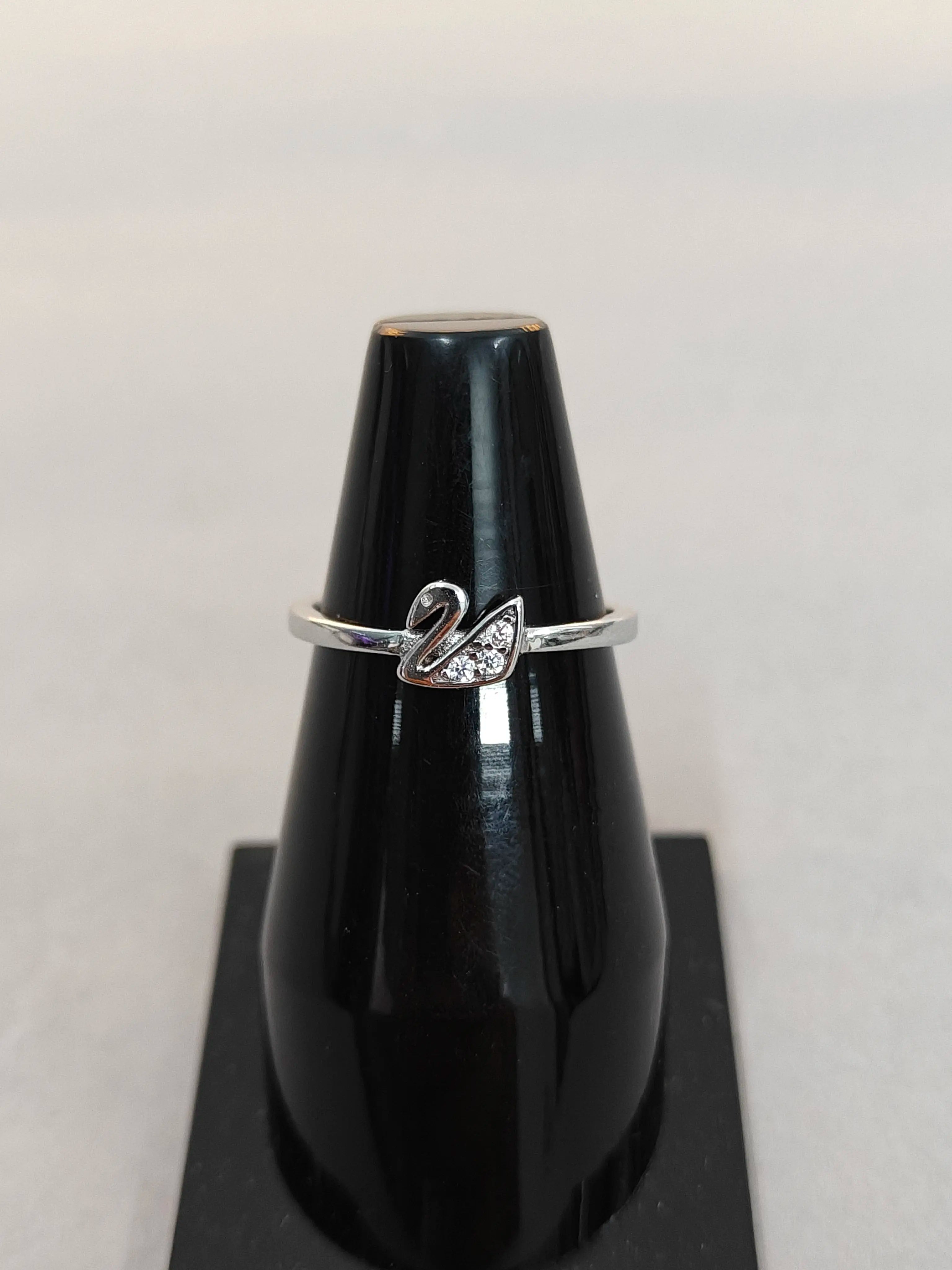 Silver ring with a swan design on a black stand against a light background