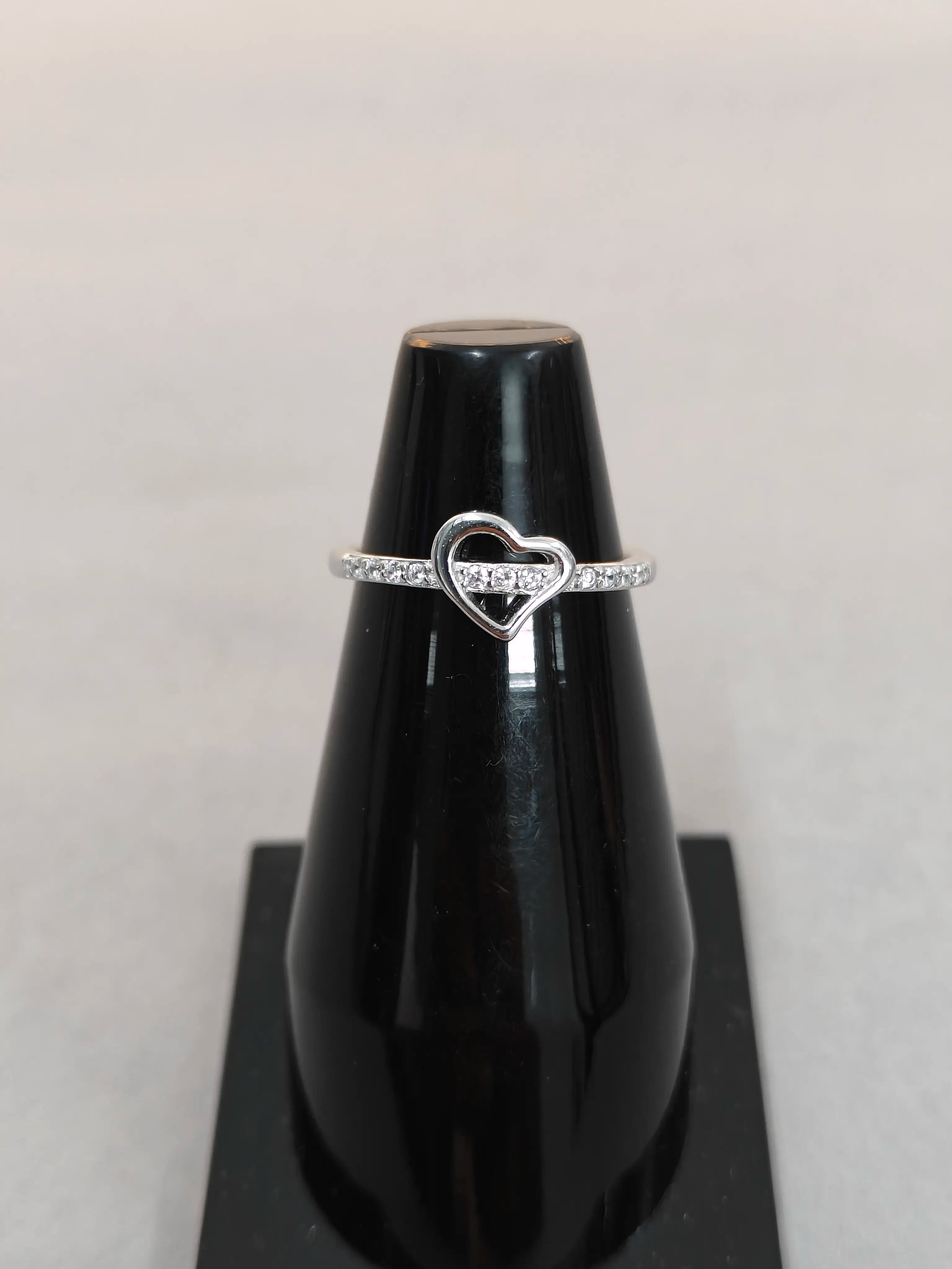 Silver ring with a heart design on a black stand against a light gray background