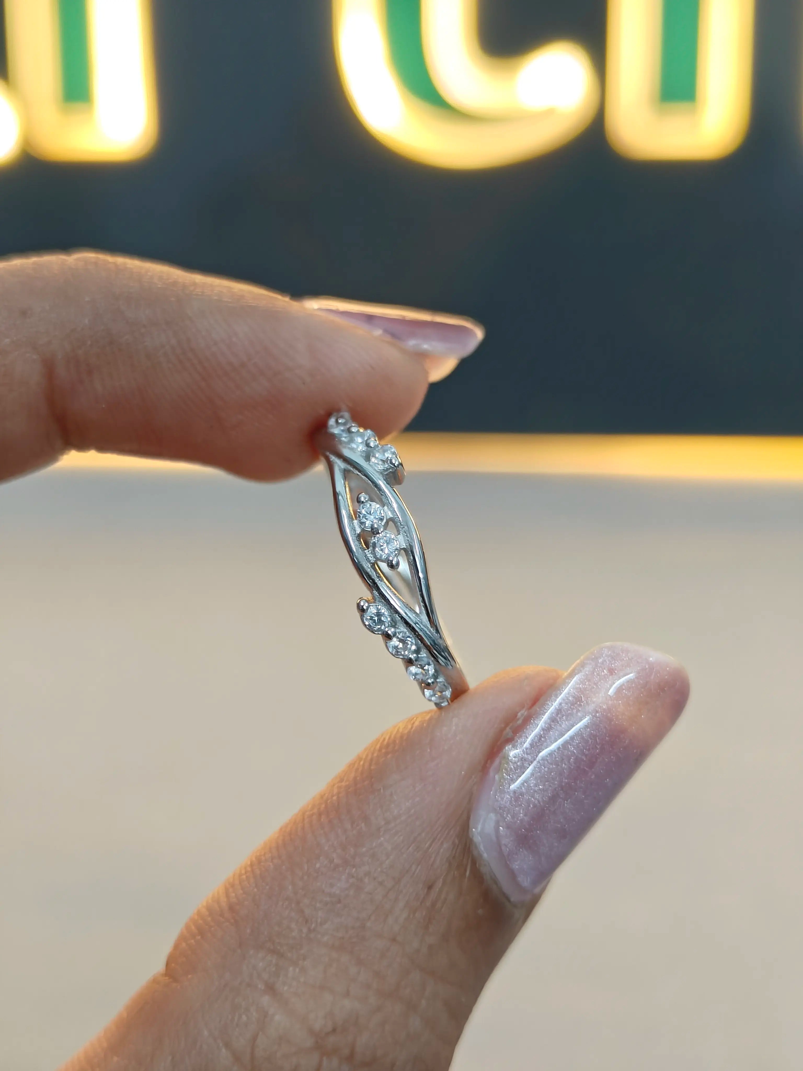 Silver ring with diamonds held by a hand against a blurred background