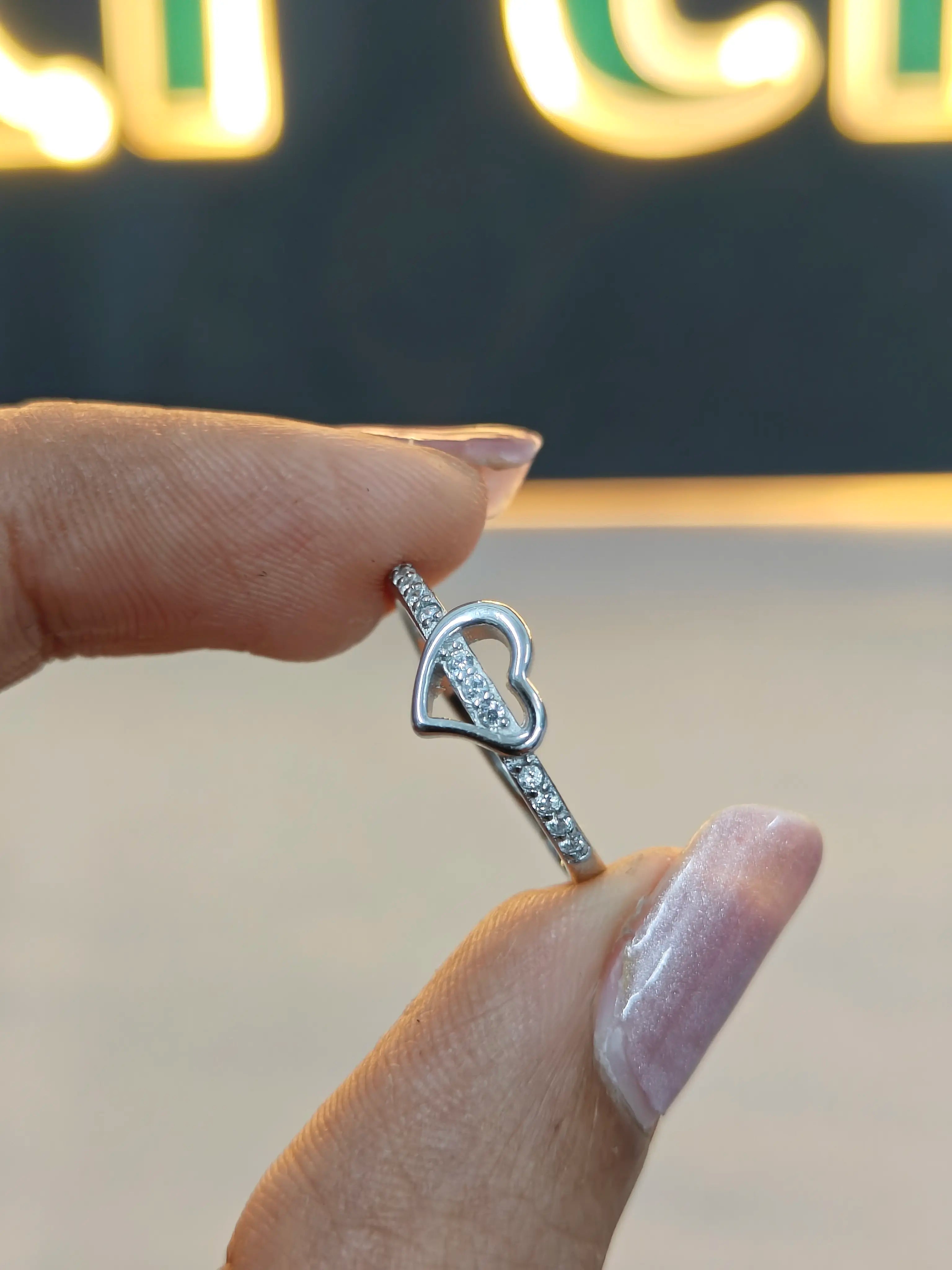 Silver ring with a heart design on a finger against a blurred background