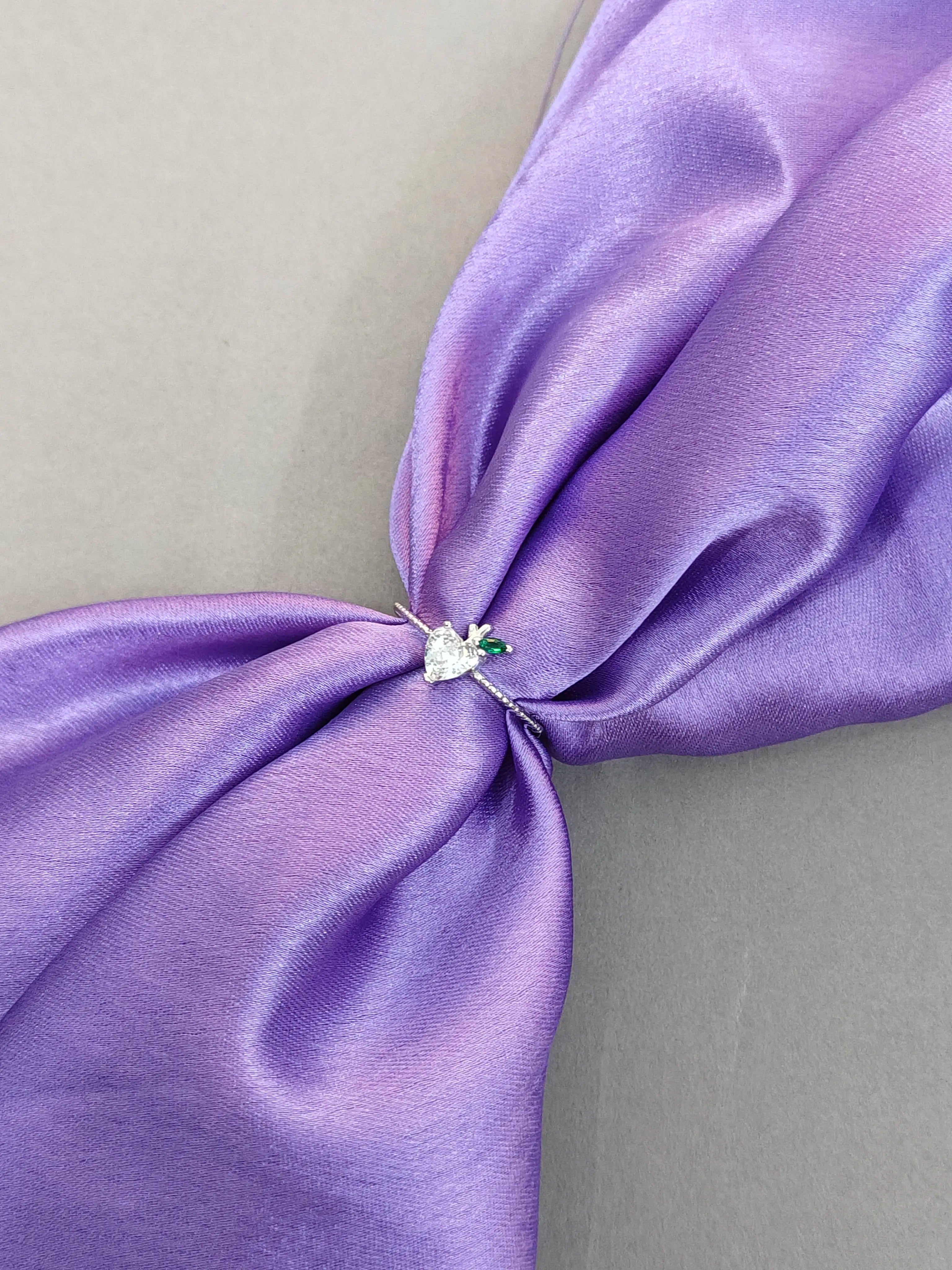 Close-up of a purple satin bow with a decorative pin on a light gray background