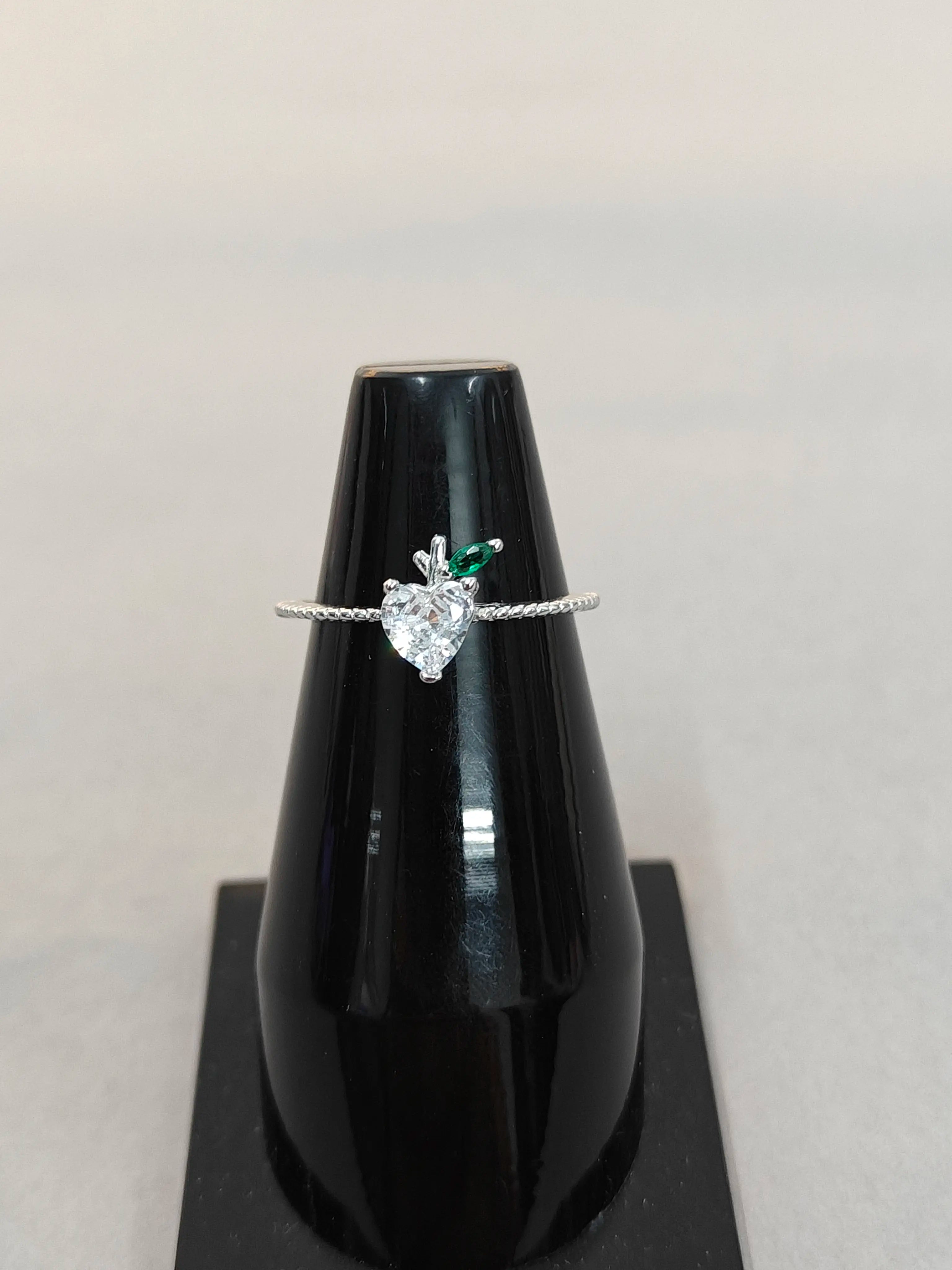 Heart-shaped diamond ring on a black stand with a white background