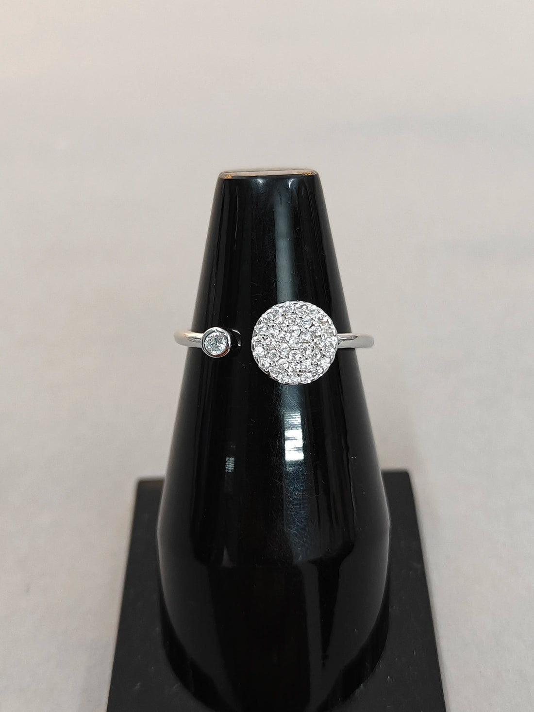 Silver ring with a diamond on a black stand against a light gray background