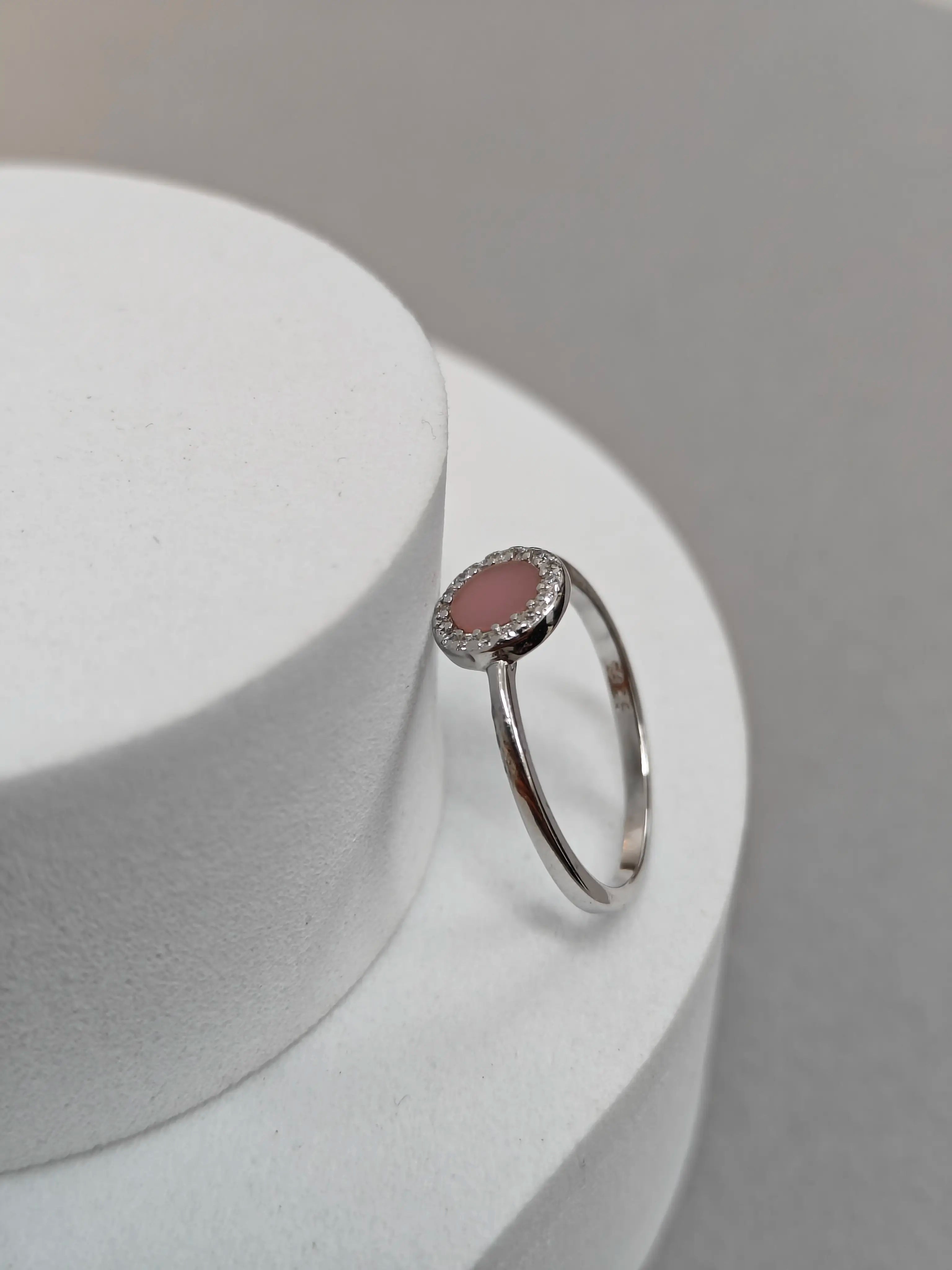 Silver ring with a pink gemstone on a white pedestal against a gray background