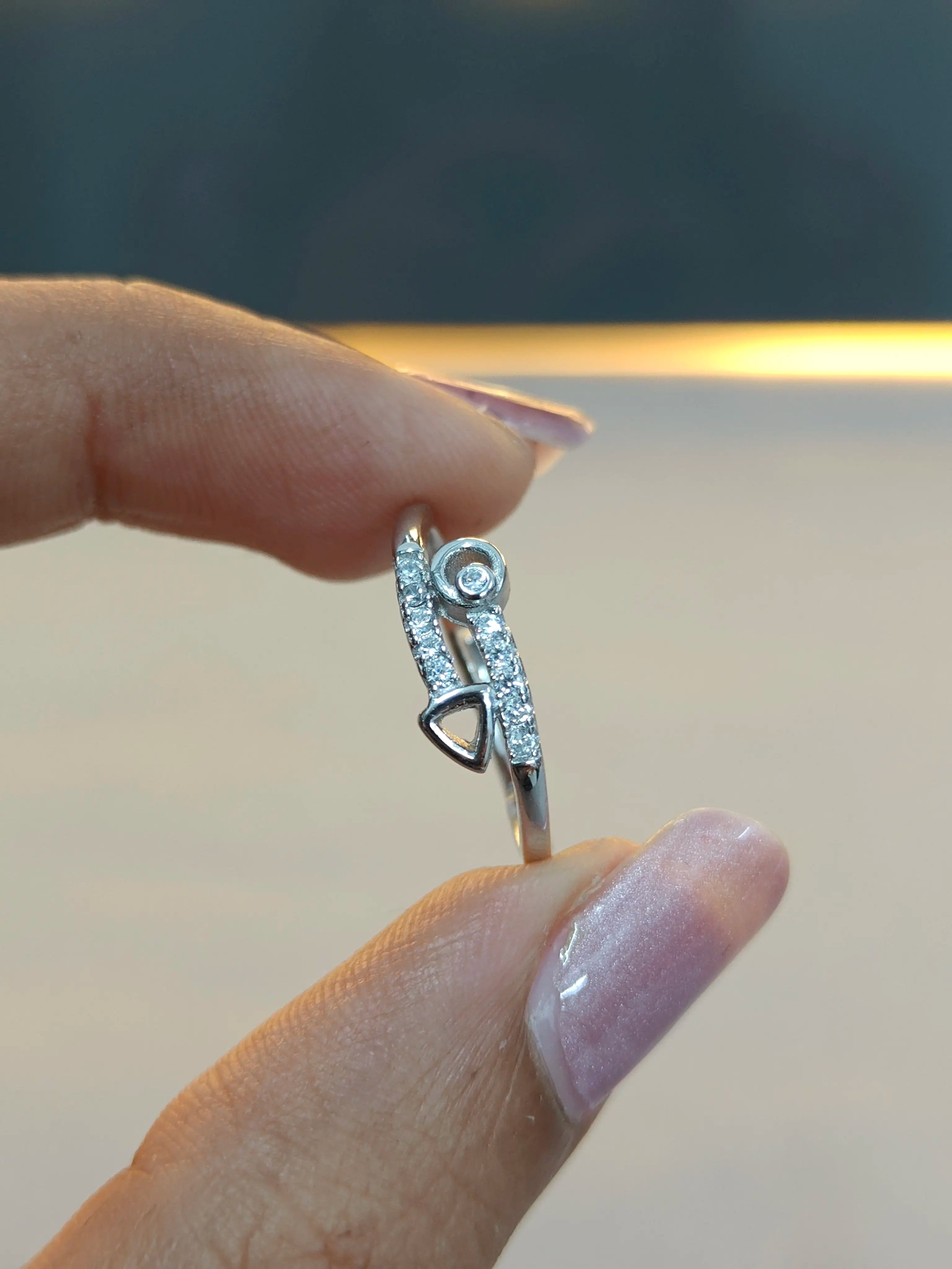Silver ring with diamonds held between fingers against a neutral background