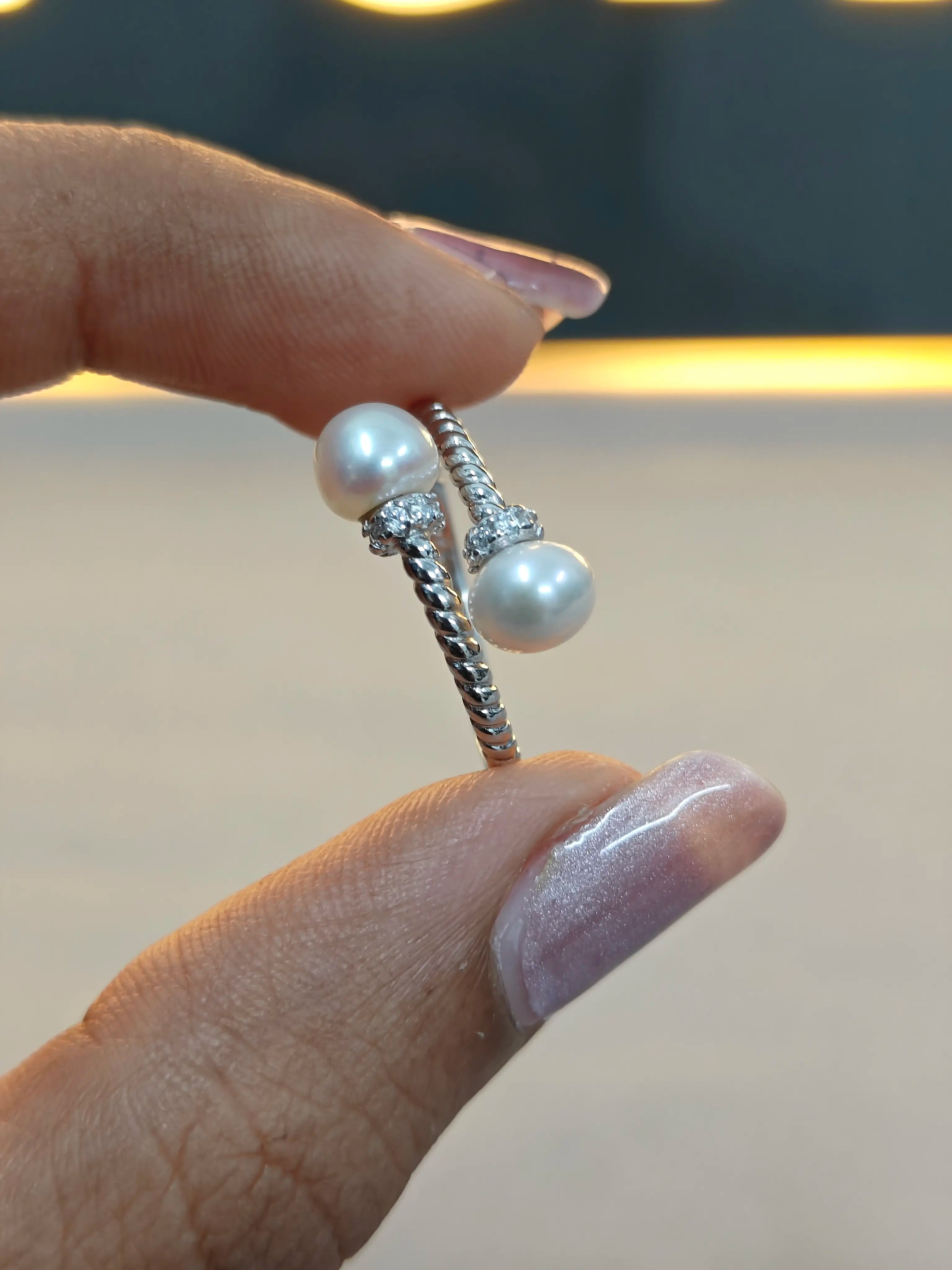 Pearl and silver ring held between fingers against a neutral background