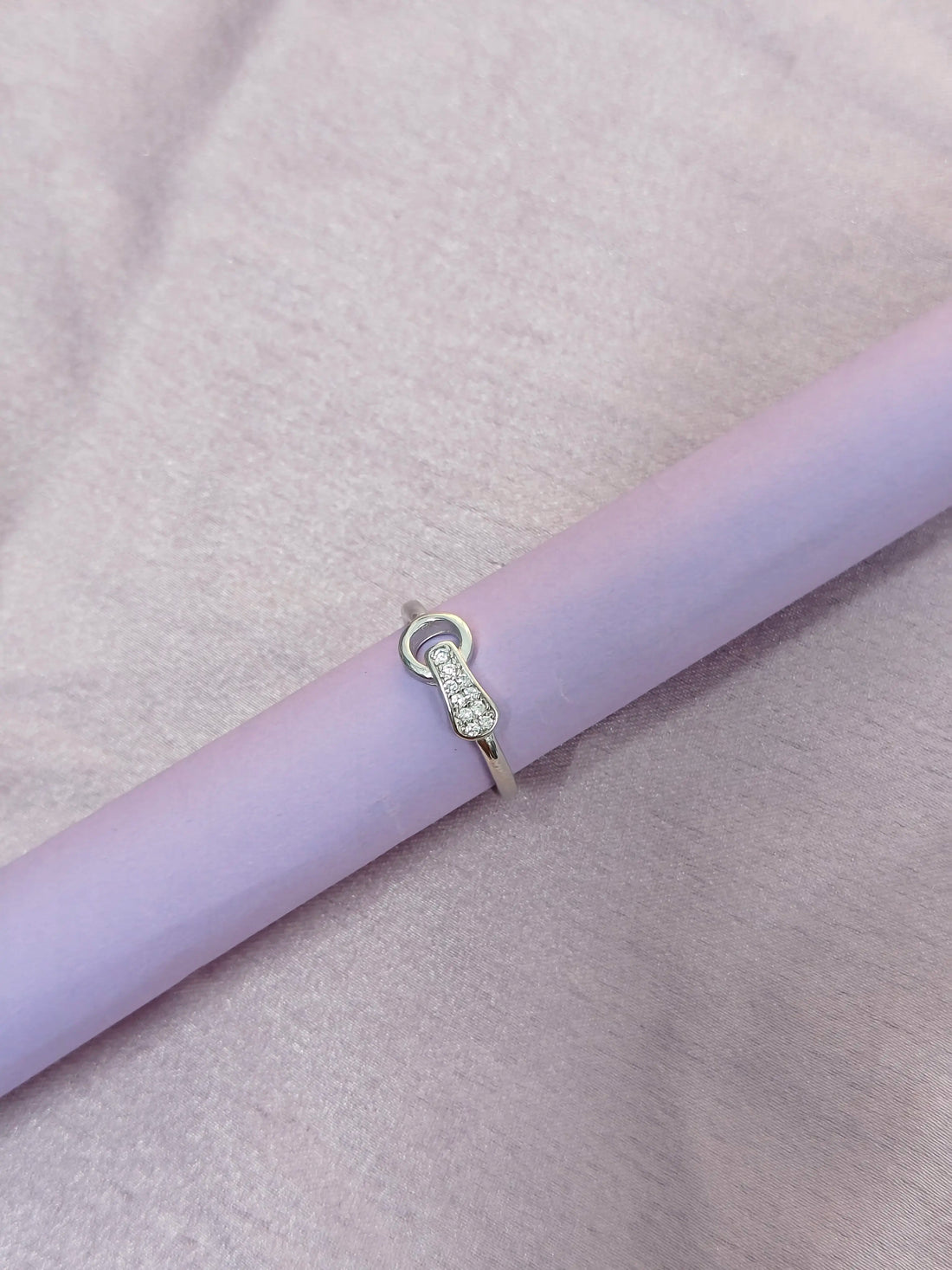 Silver ring with diamonds on a light purple surface