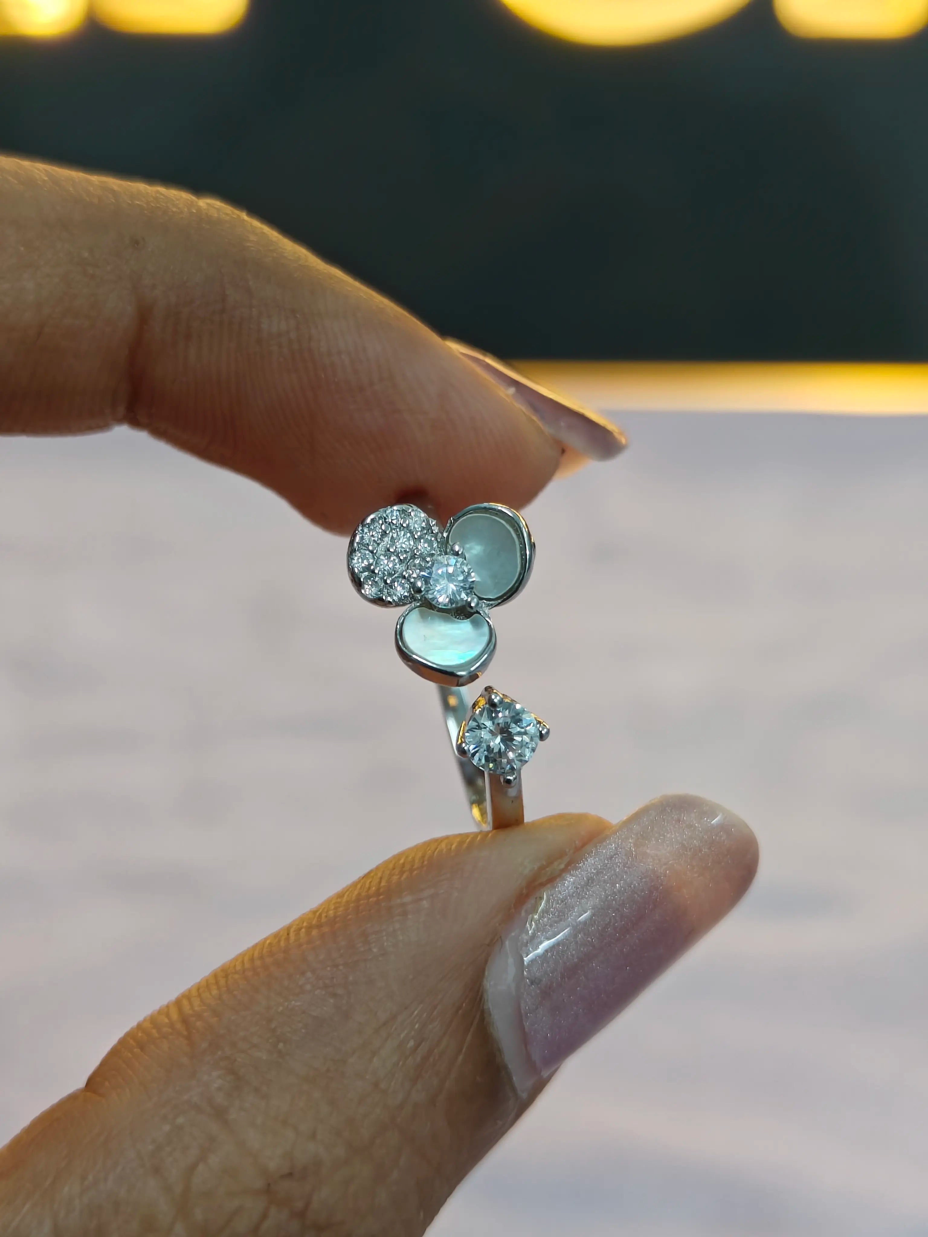 Close-up of a hand holding a silver ring with gemstones against a blurred background