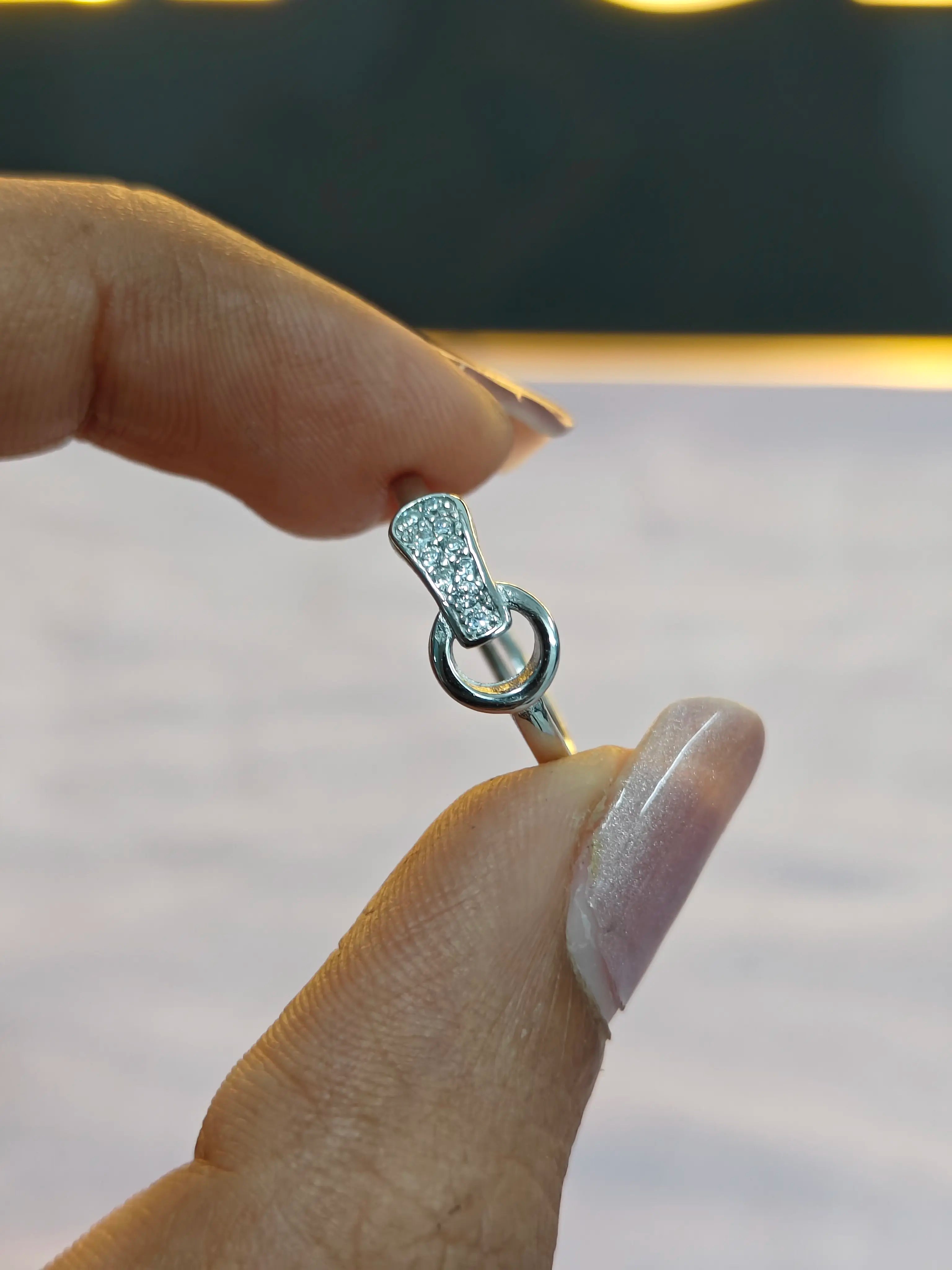 Silver ring with gemstones held between fingers against a neutral background