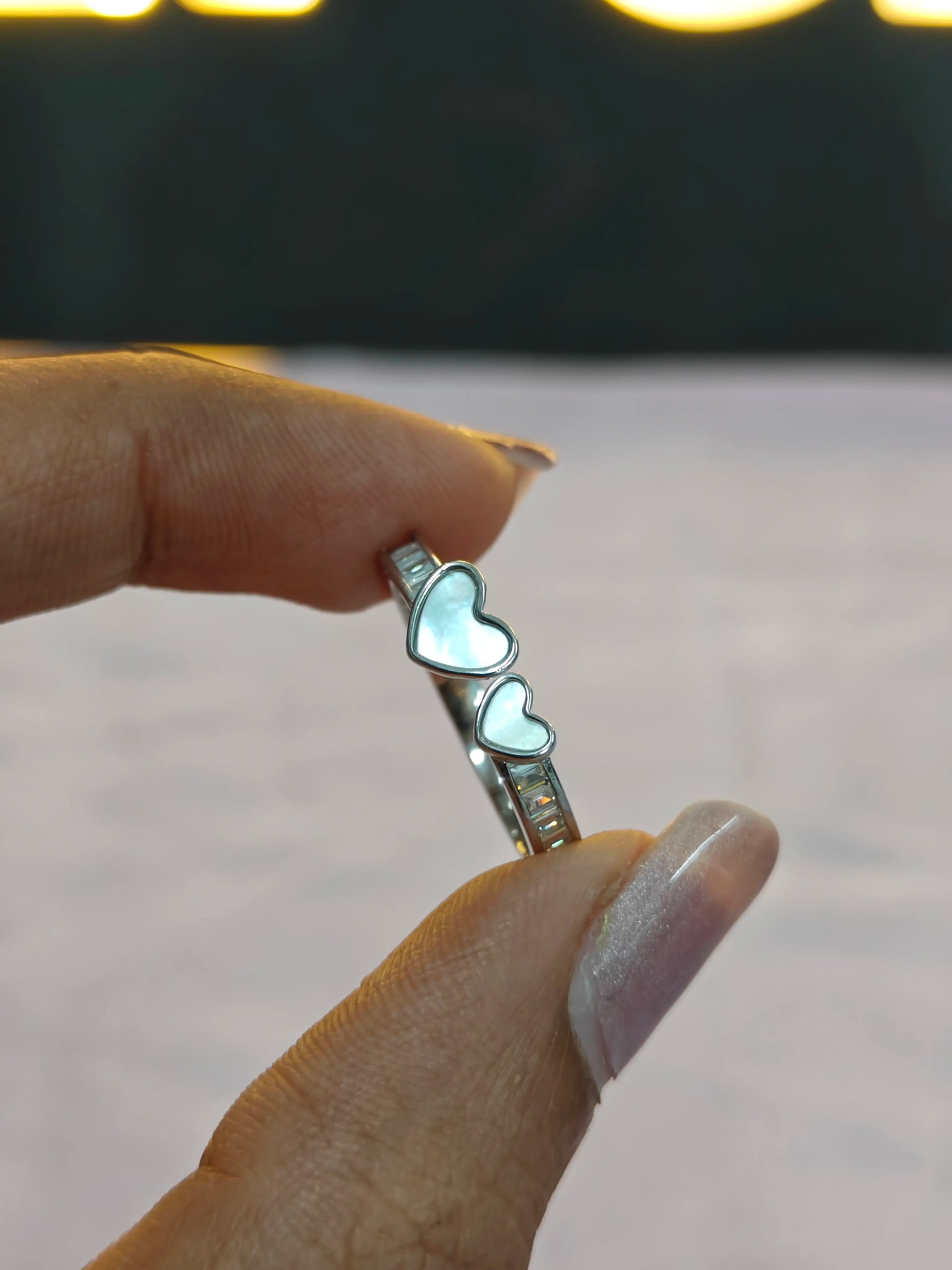 Silver ring with heart-shaped stones held by a hand against a blurred background