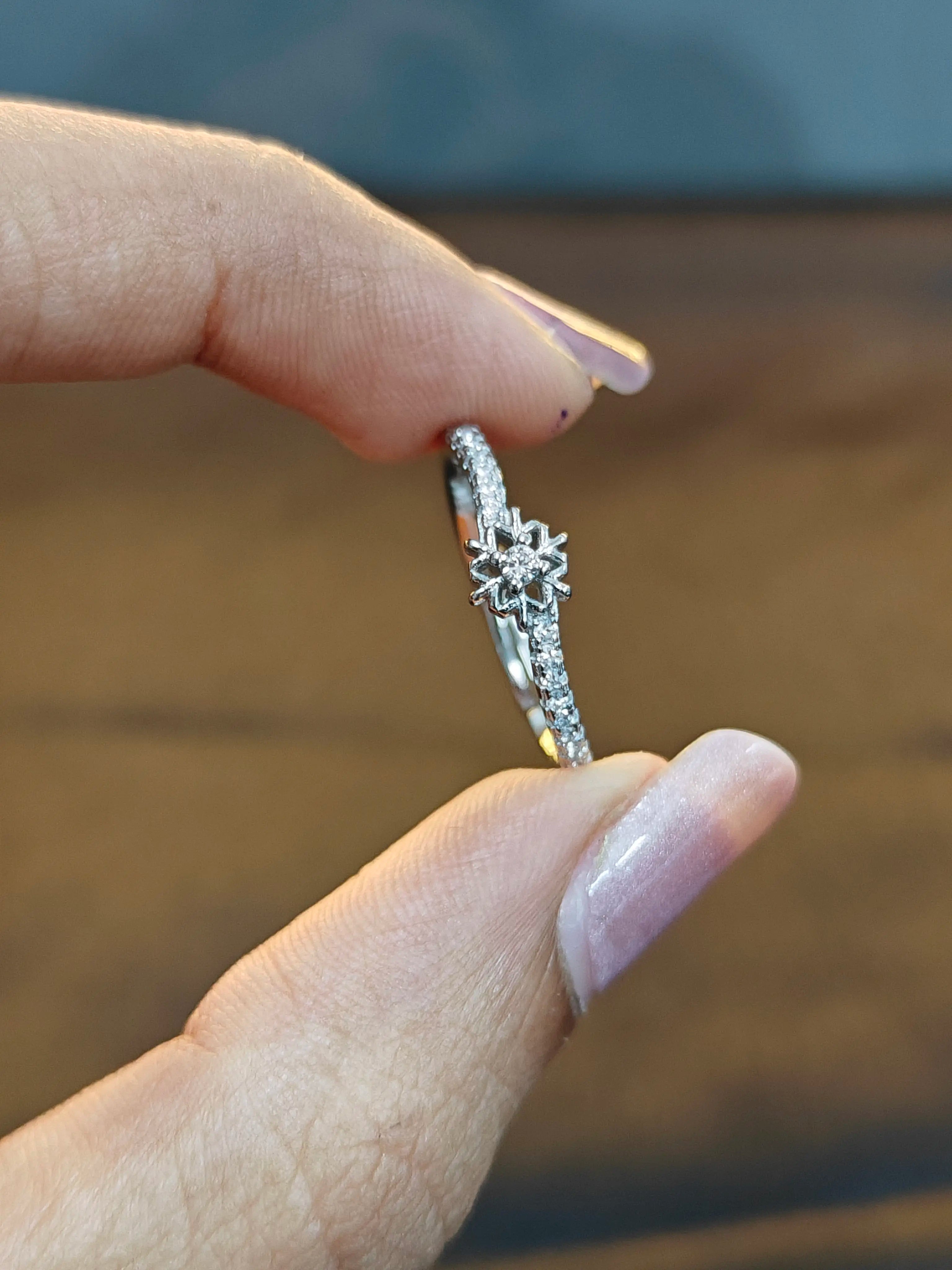 Silver ring with floral design held between fingers against a blurred background