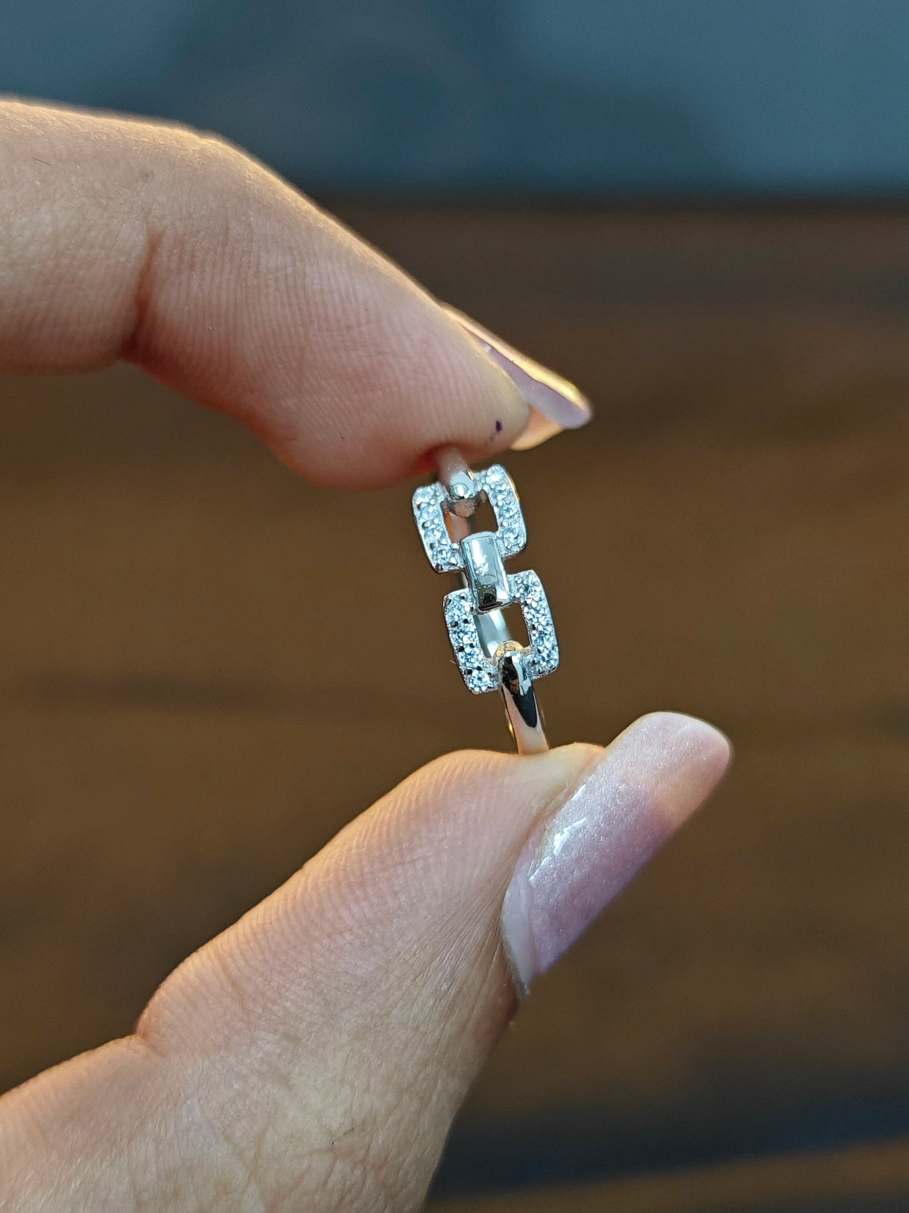 Silver ring with diamonds held between fingers against a blurred background