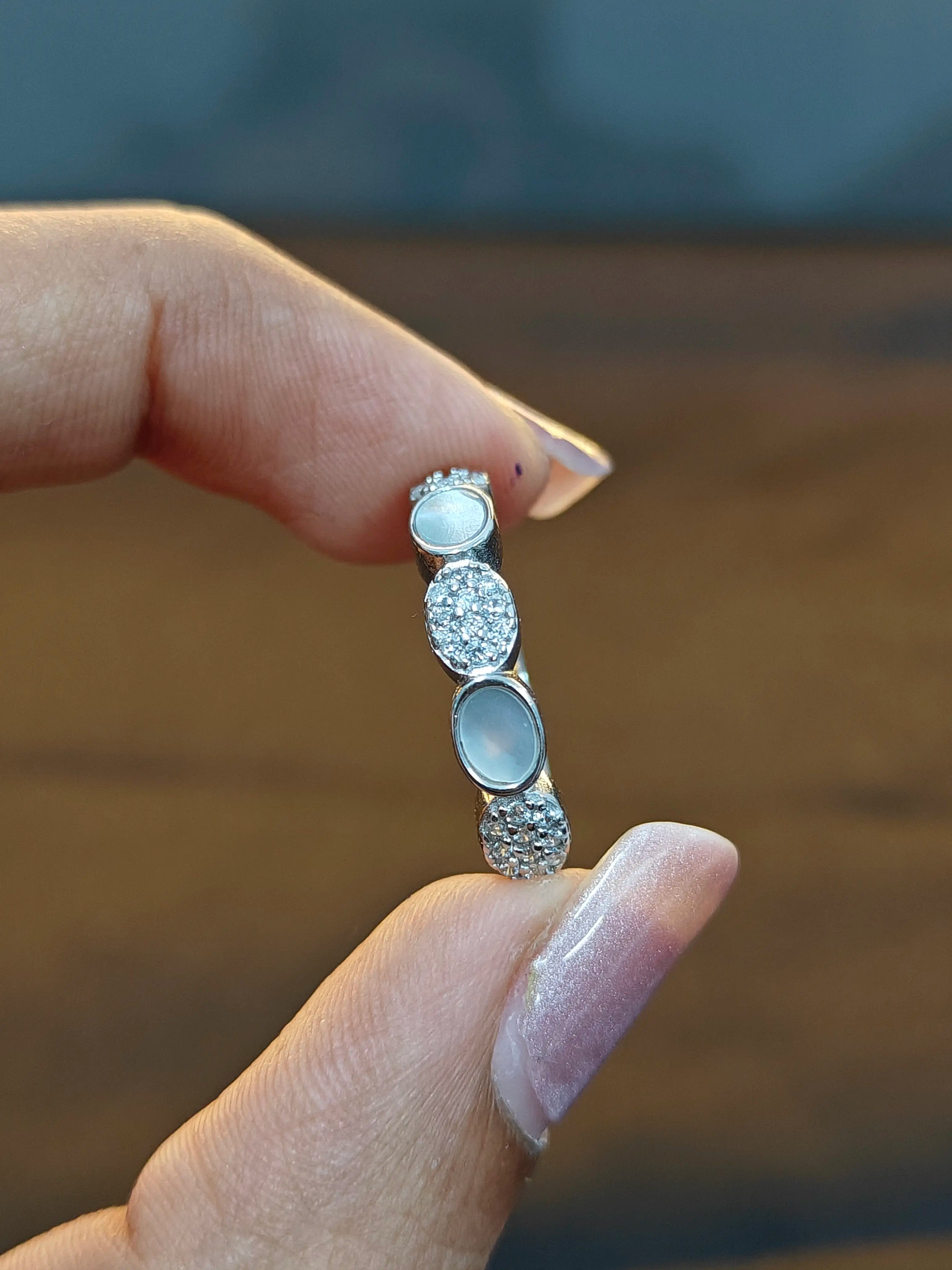 Silver ring with gemstones held between fingers against a blurred background