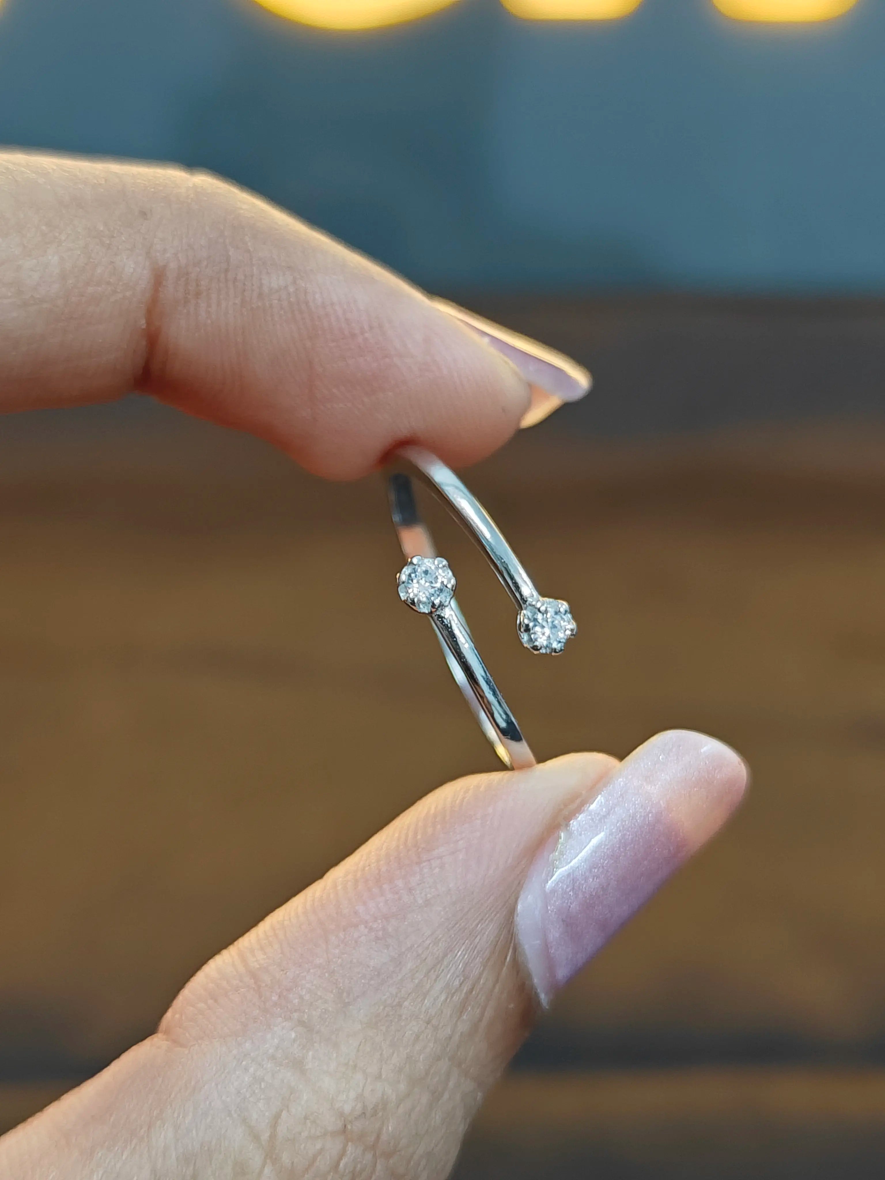 Silver earrings with clear stones held between fingers against a blurred background