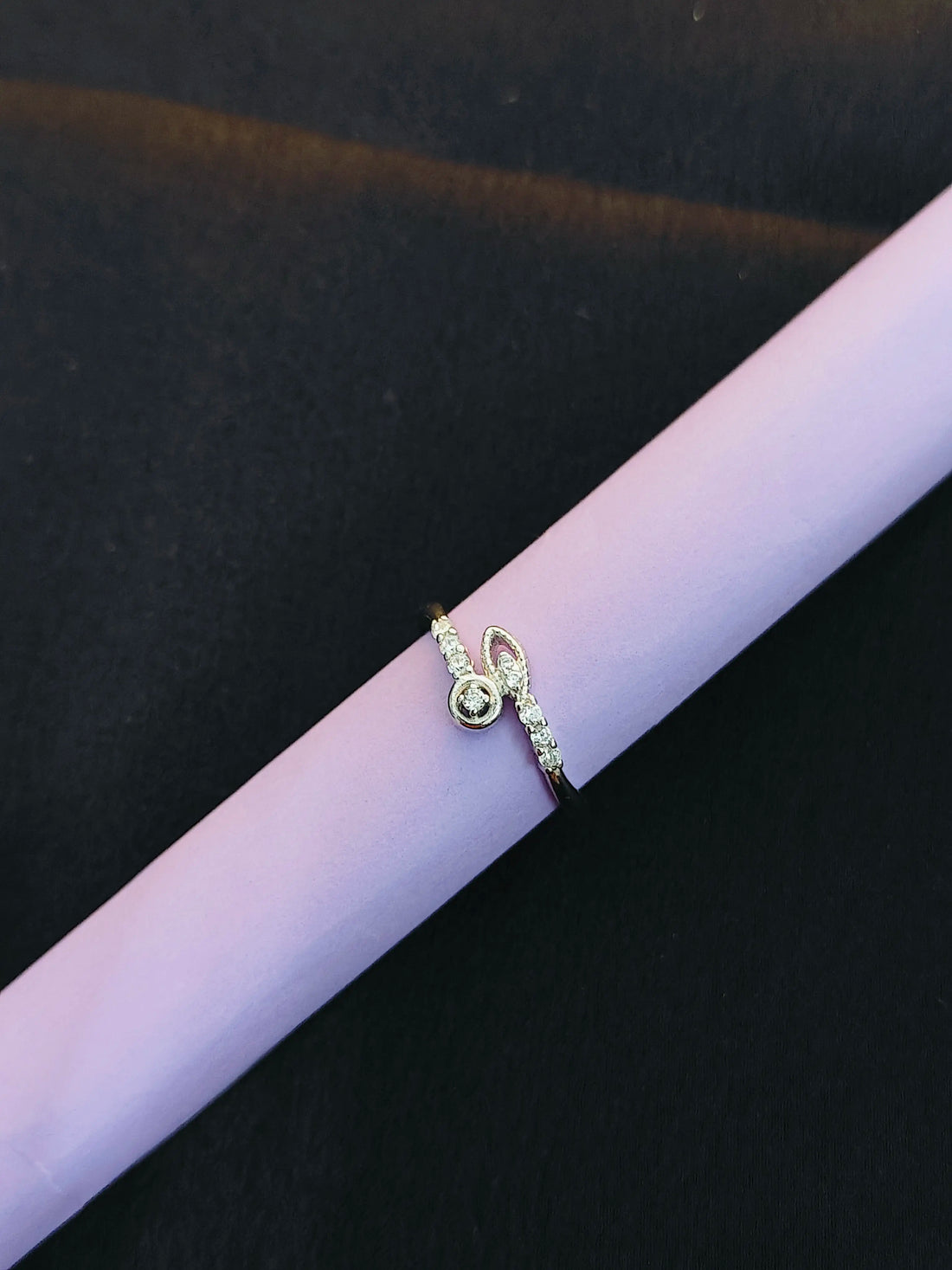 Gold ring with small diamonds on a purple cylindrical object against a black background