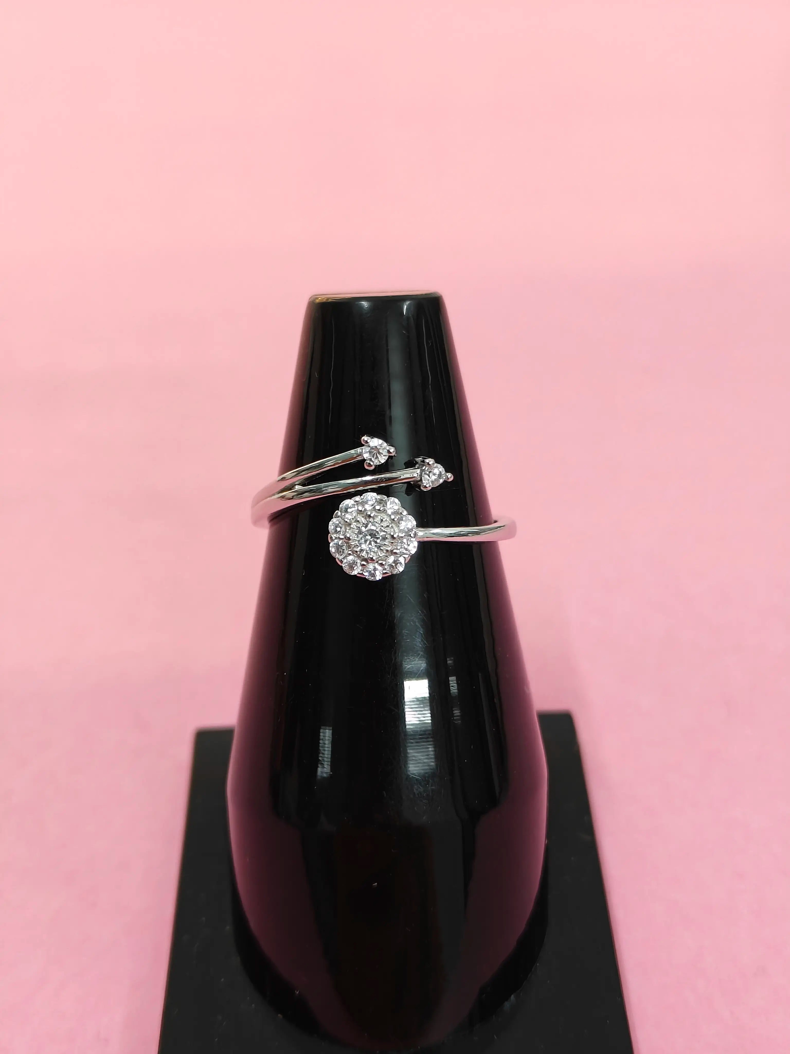 Silver ring with a circular design on a black stand against a pink background