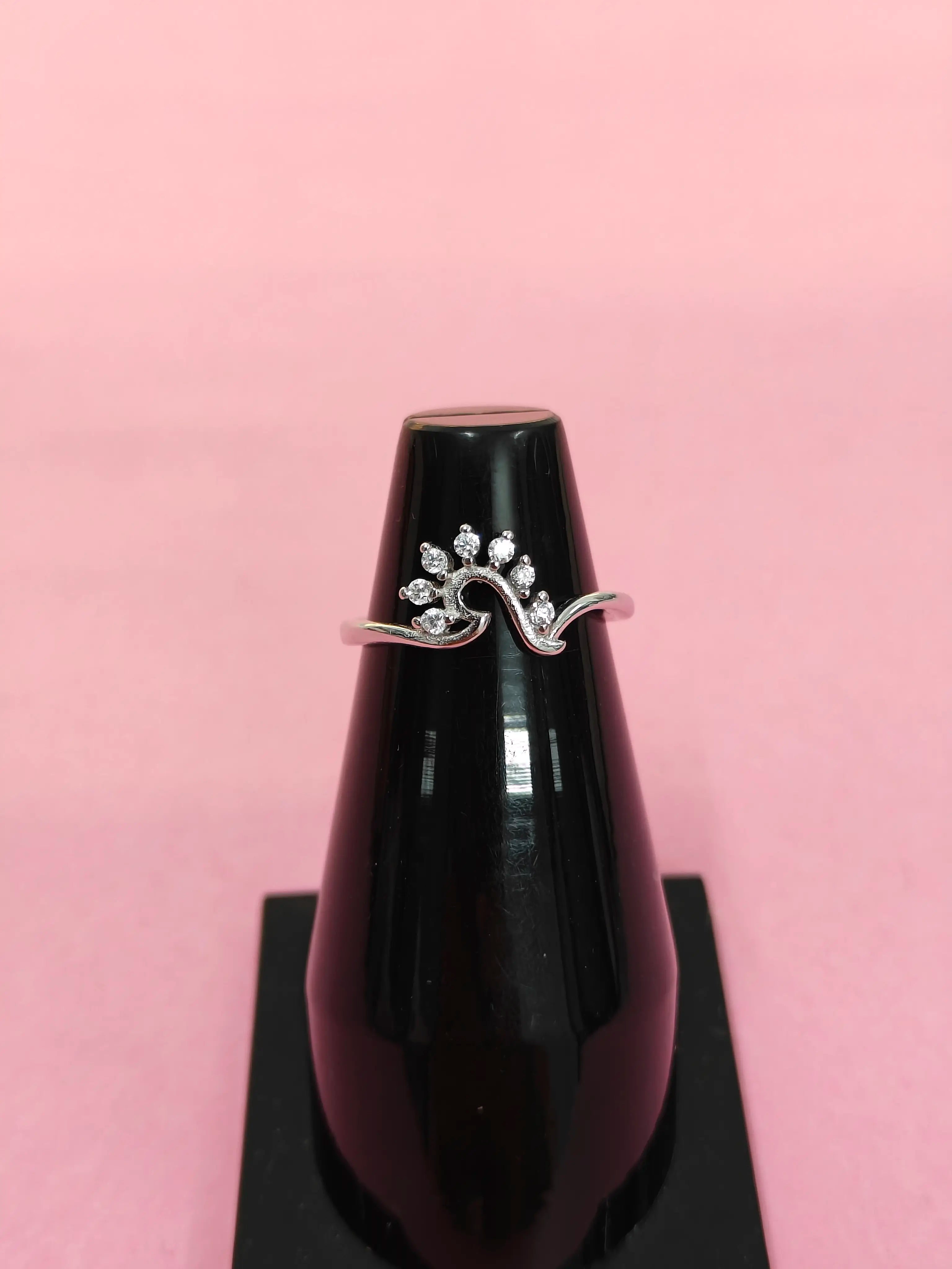 Silver ring with gemstones on a black stand against a pink background