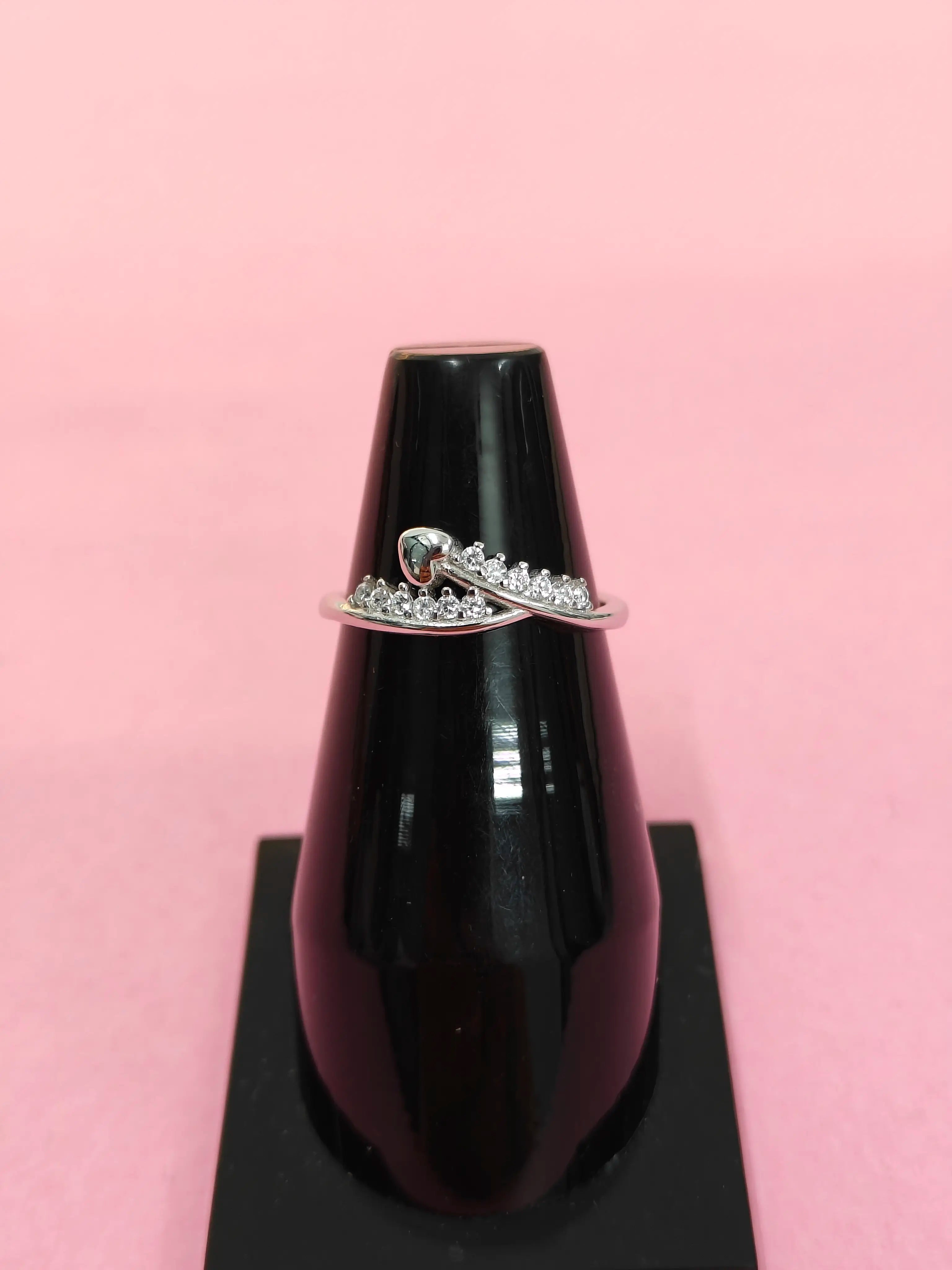 Black lip gloss with a silver ring featuring a heart and small stones on a pink background