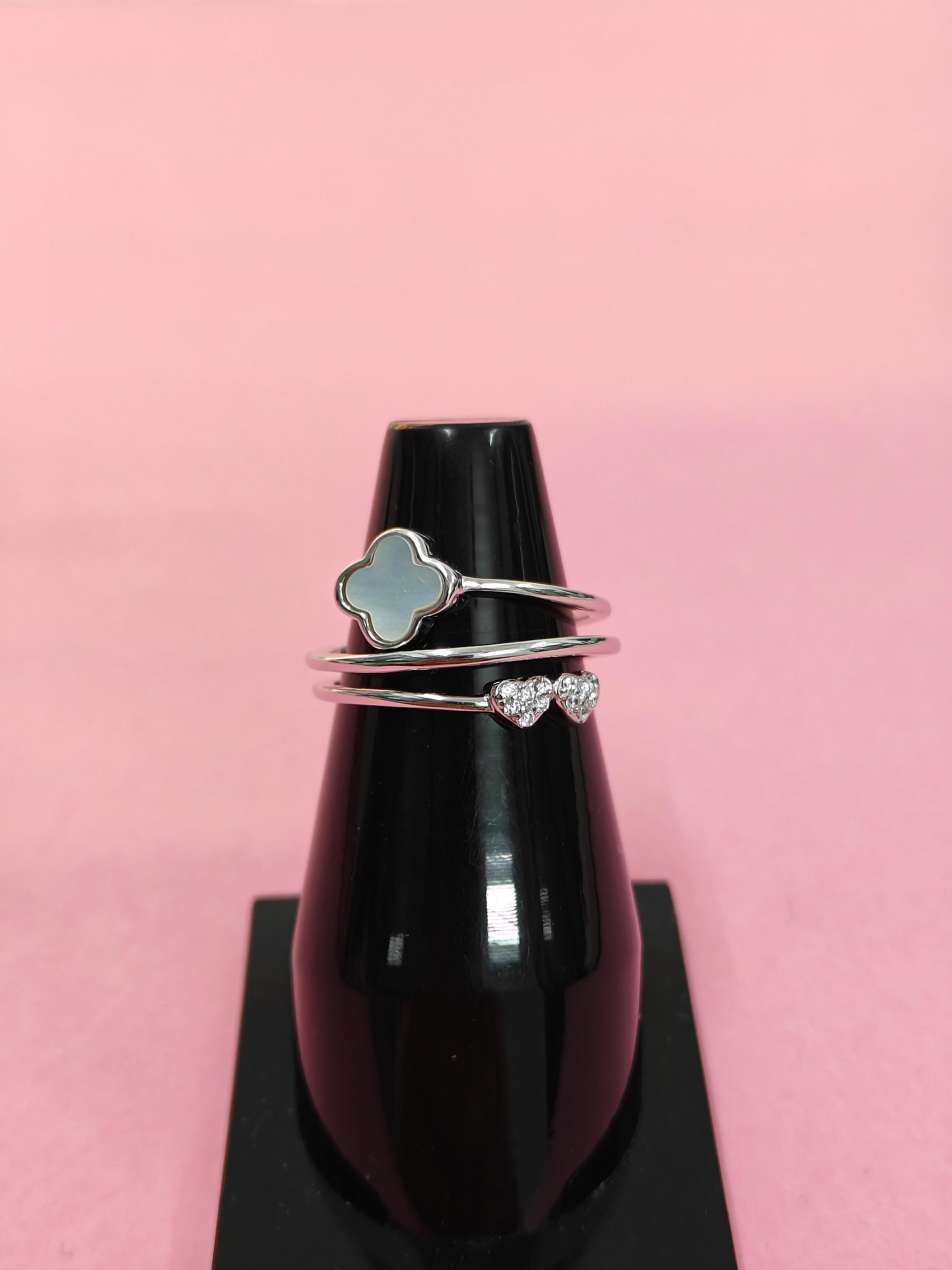 Three silver rings with different designs on a black bottle against a pink background
