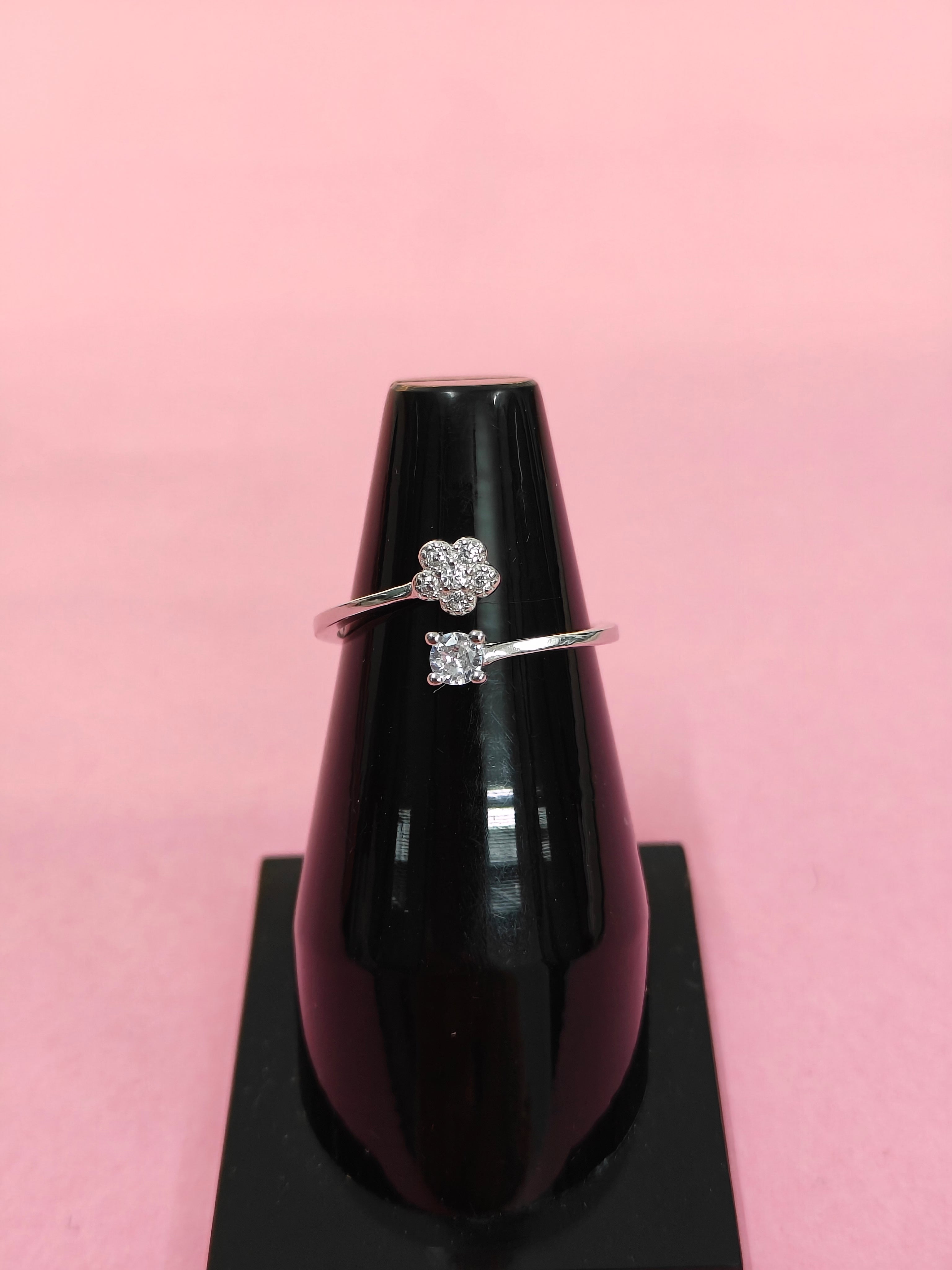 Silver ring with a diamond on a black stand against a pink background