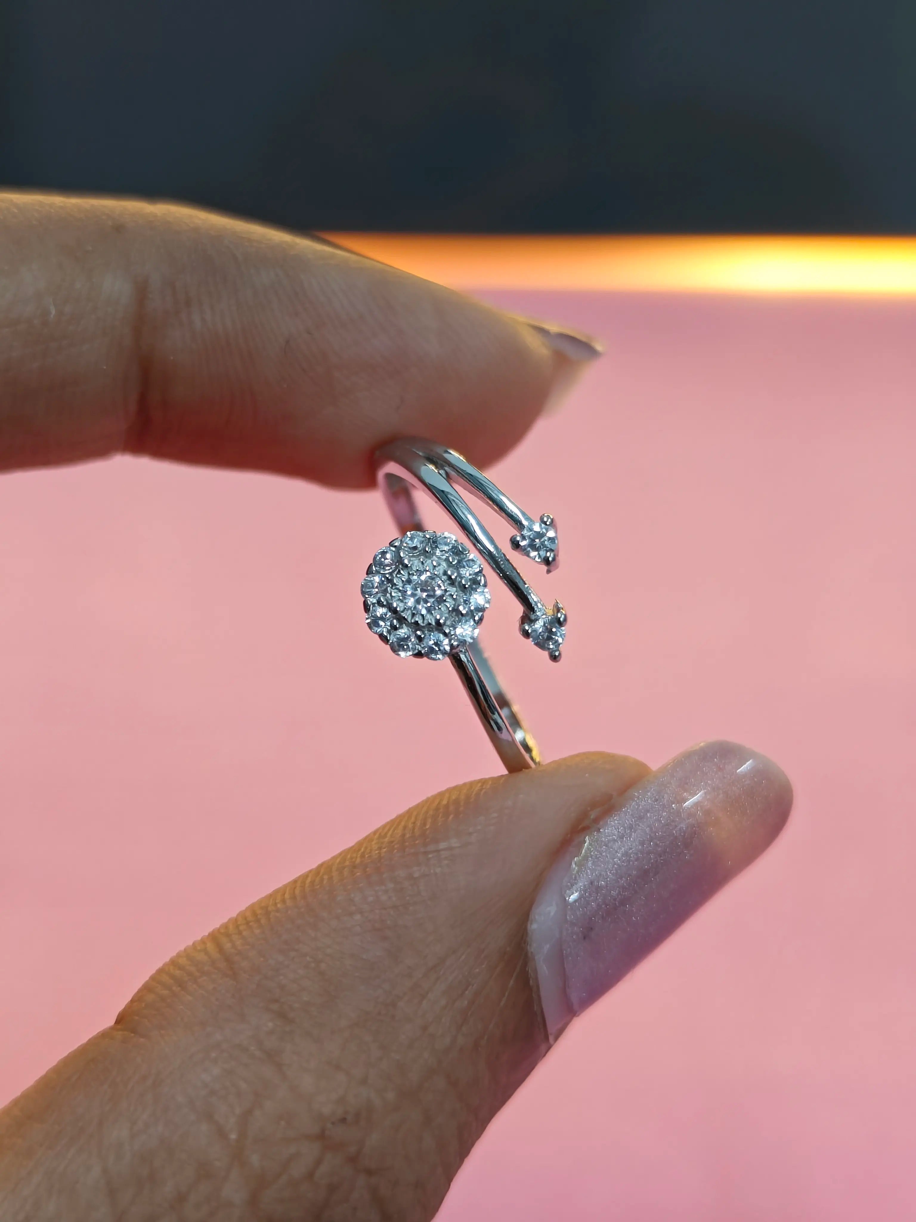 Silver ring with a diamond-like center held between fingers against a pink background