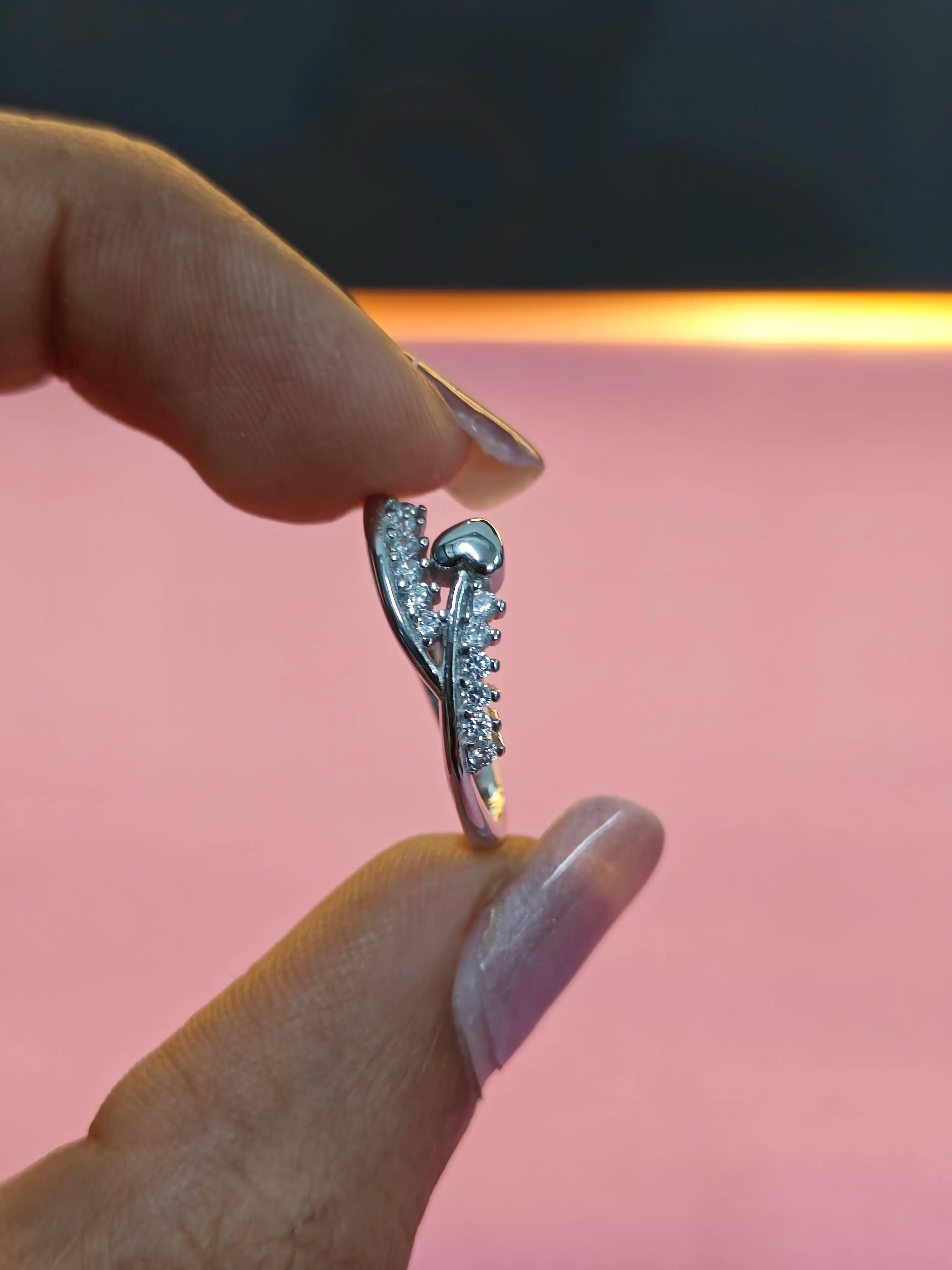 Silver ring with intricate design held between fingers against a pink background