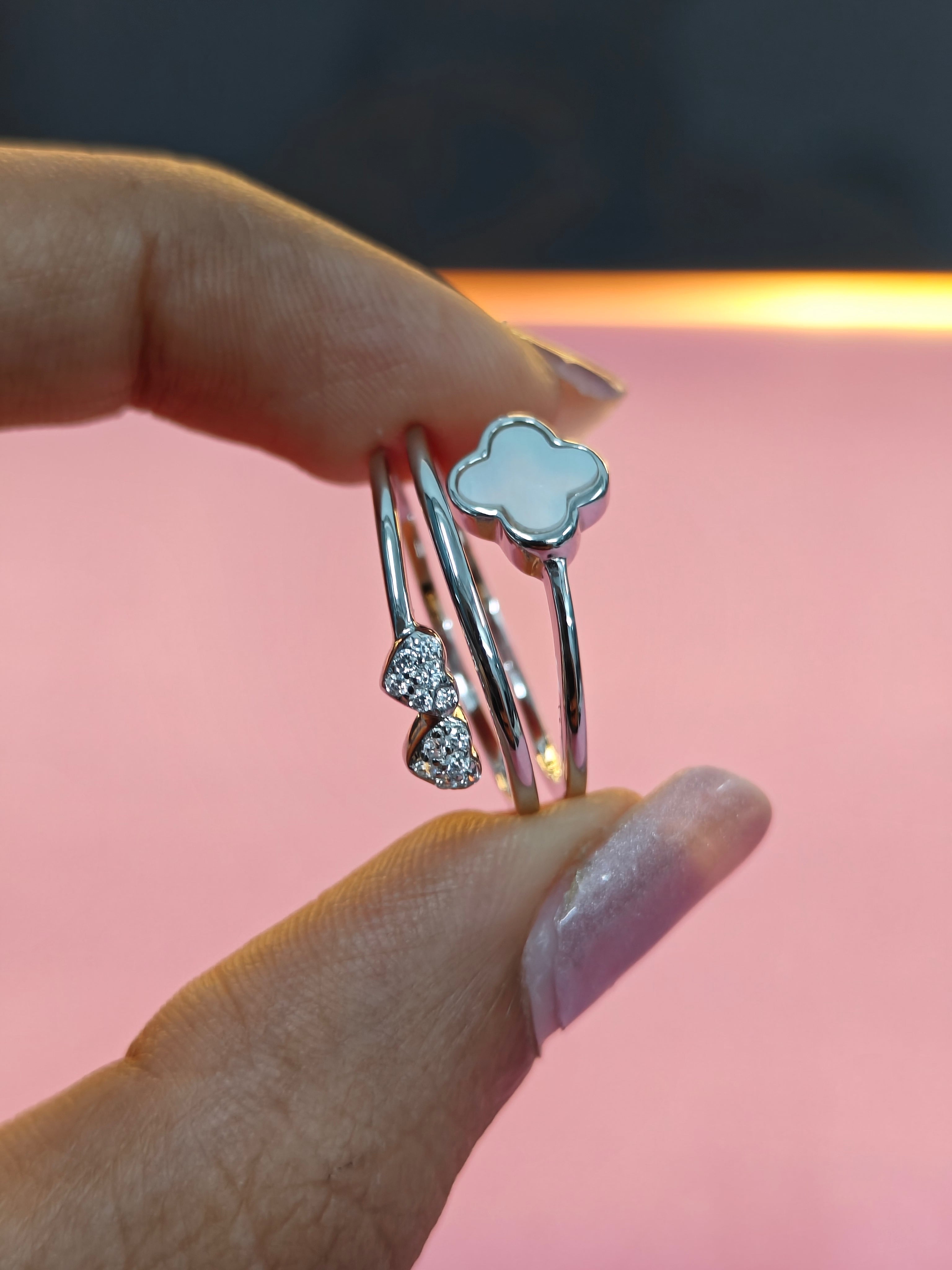 Silver rings with heart and cloud designs held by a hand against a pink background