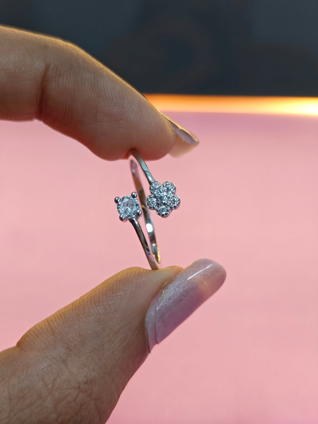 Close-up of a hand holding two diamond rings against a pink background