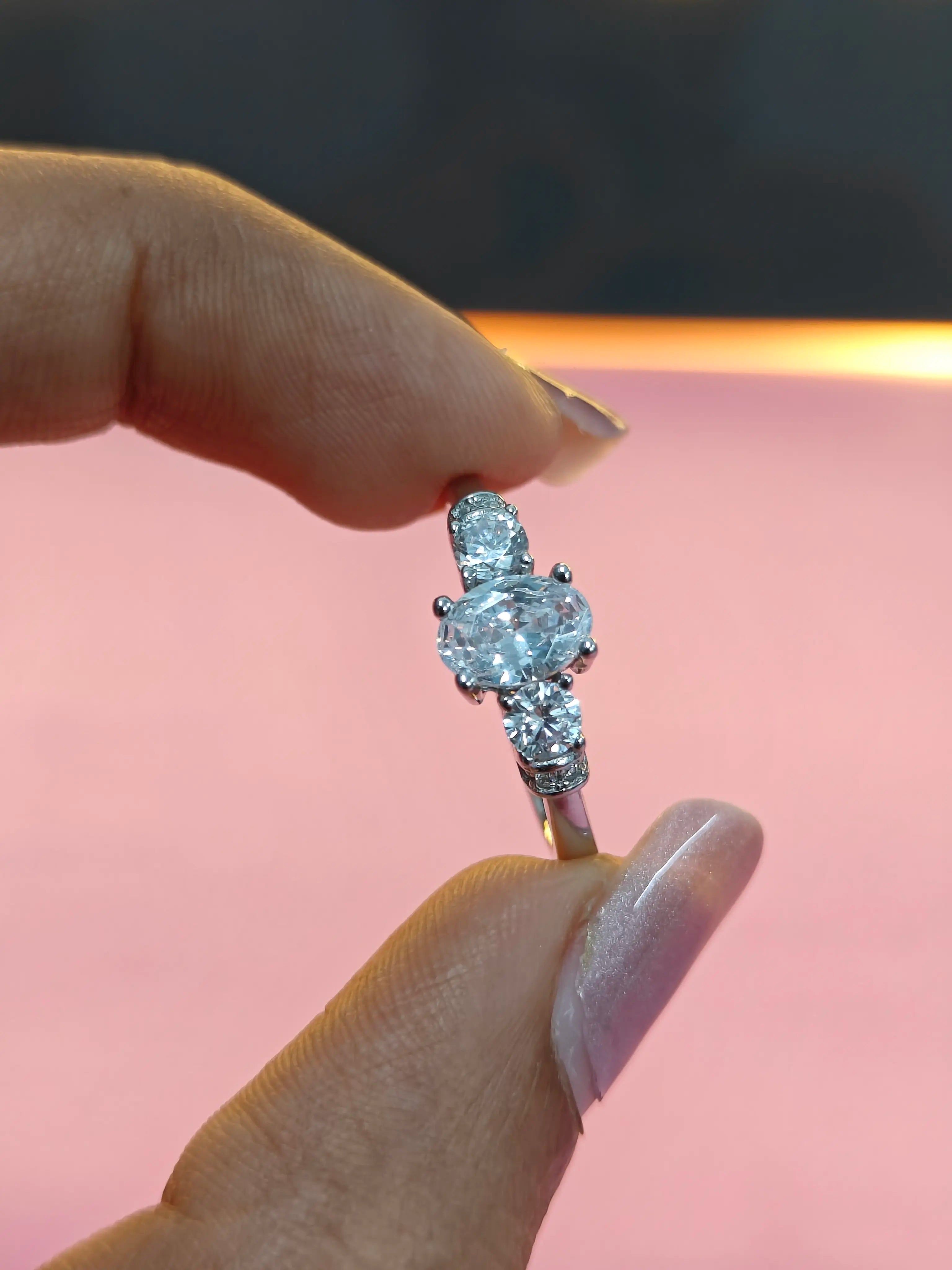 Diamond ring held between fingers against a pink background