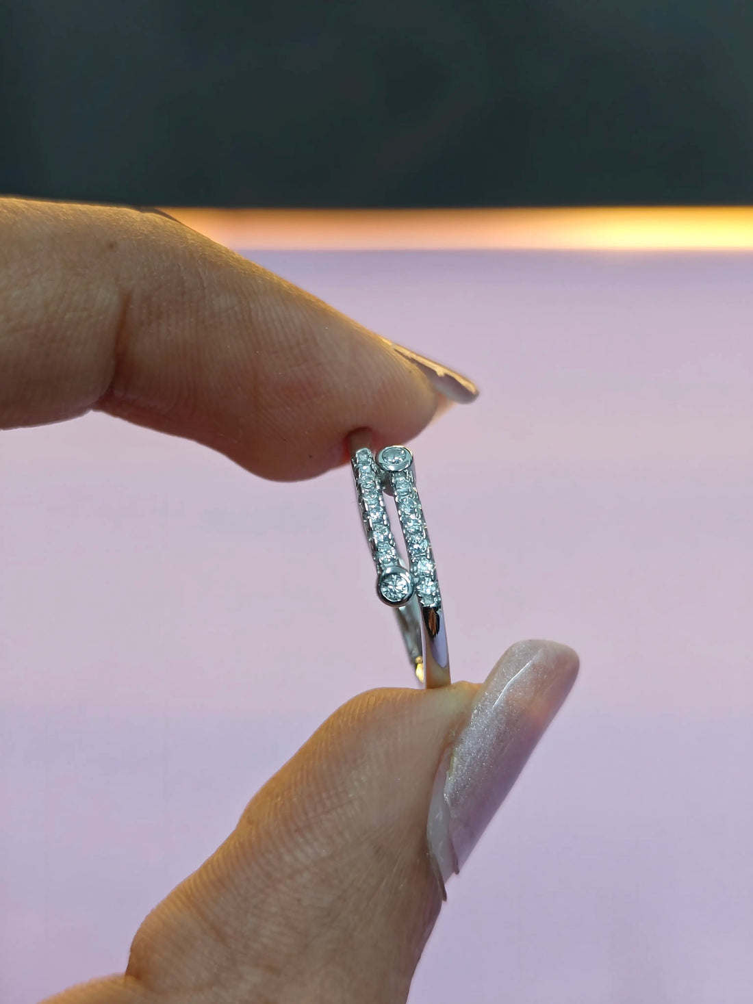 Silver ring with small diamonds held between fingers against a neutral background