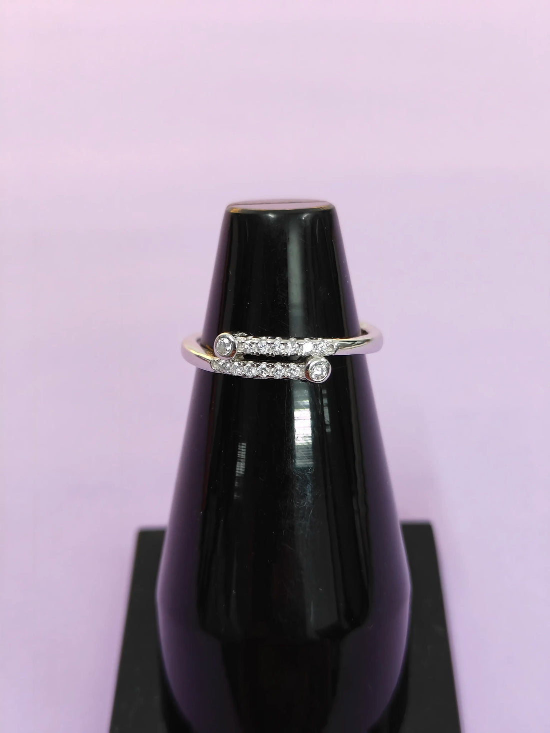 Diamond ring on a black stand against a light purple background