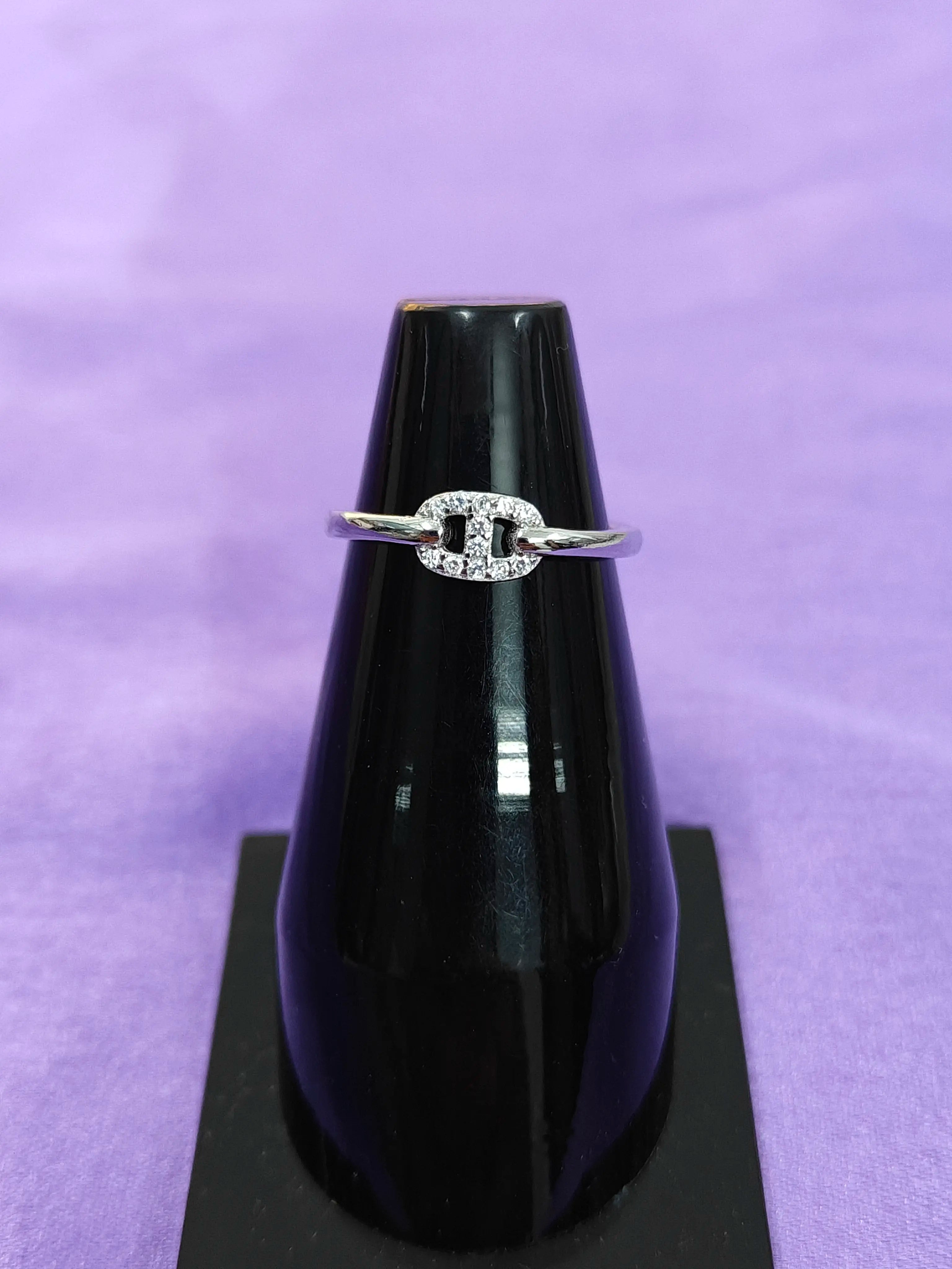 Silver ring with a diamond on a black stand against a purple background