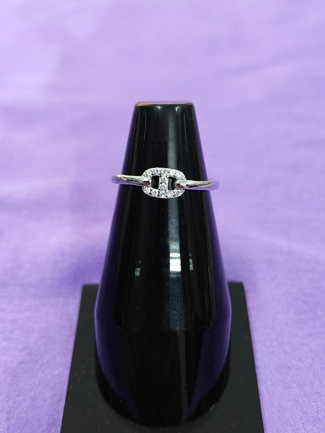 Silver ring with a diamond on a black stand against a purple background