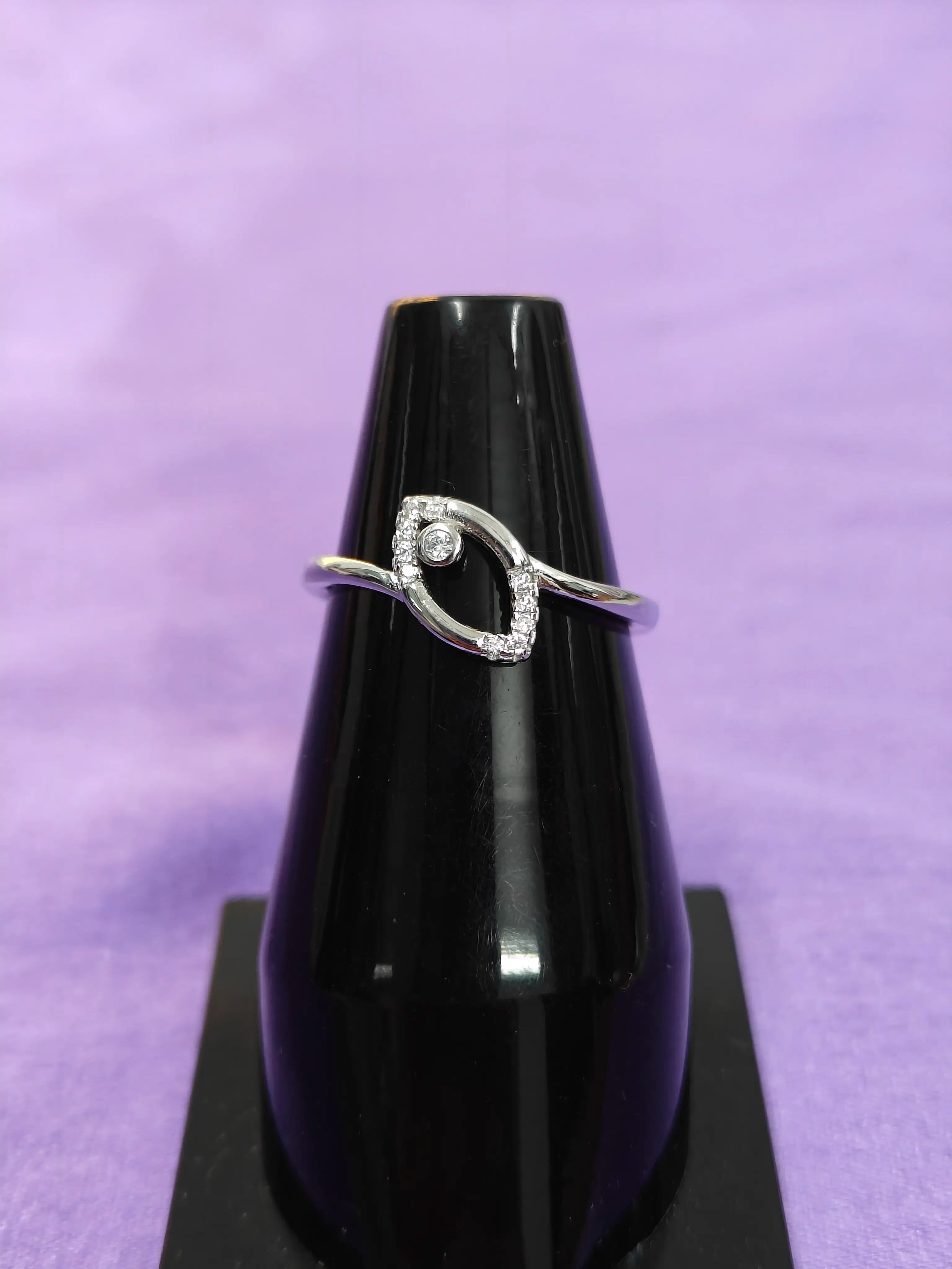 Silver ring with a diamond on a black stand against a purple background