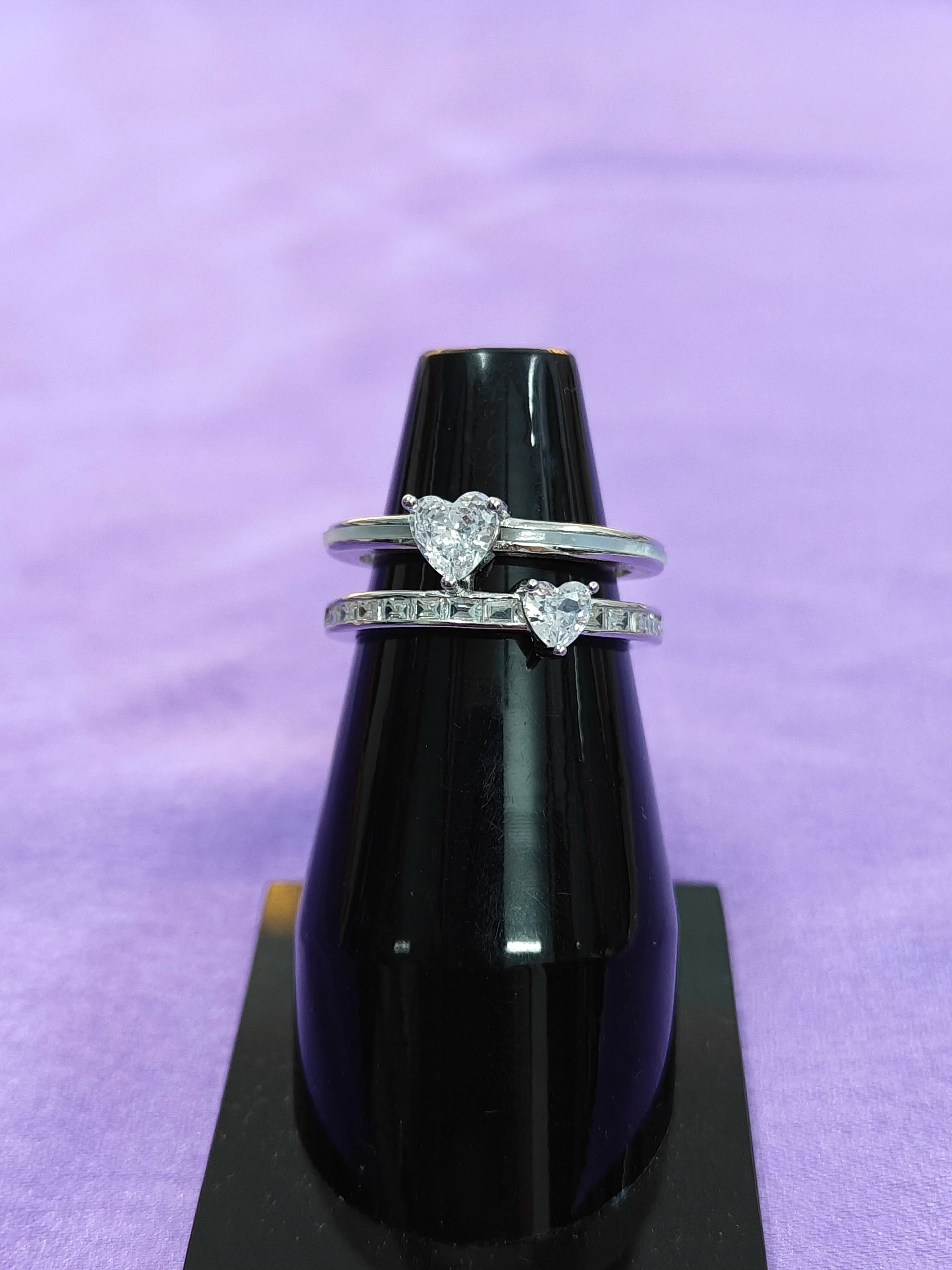 Two heart-shaped diamond rings on a black stand against a purple background