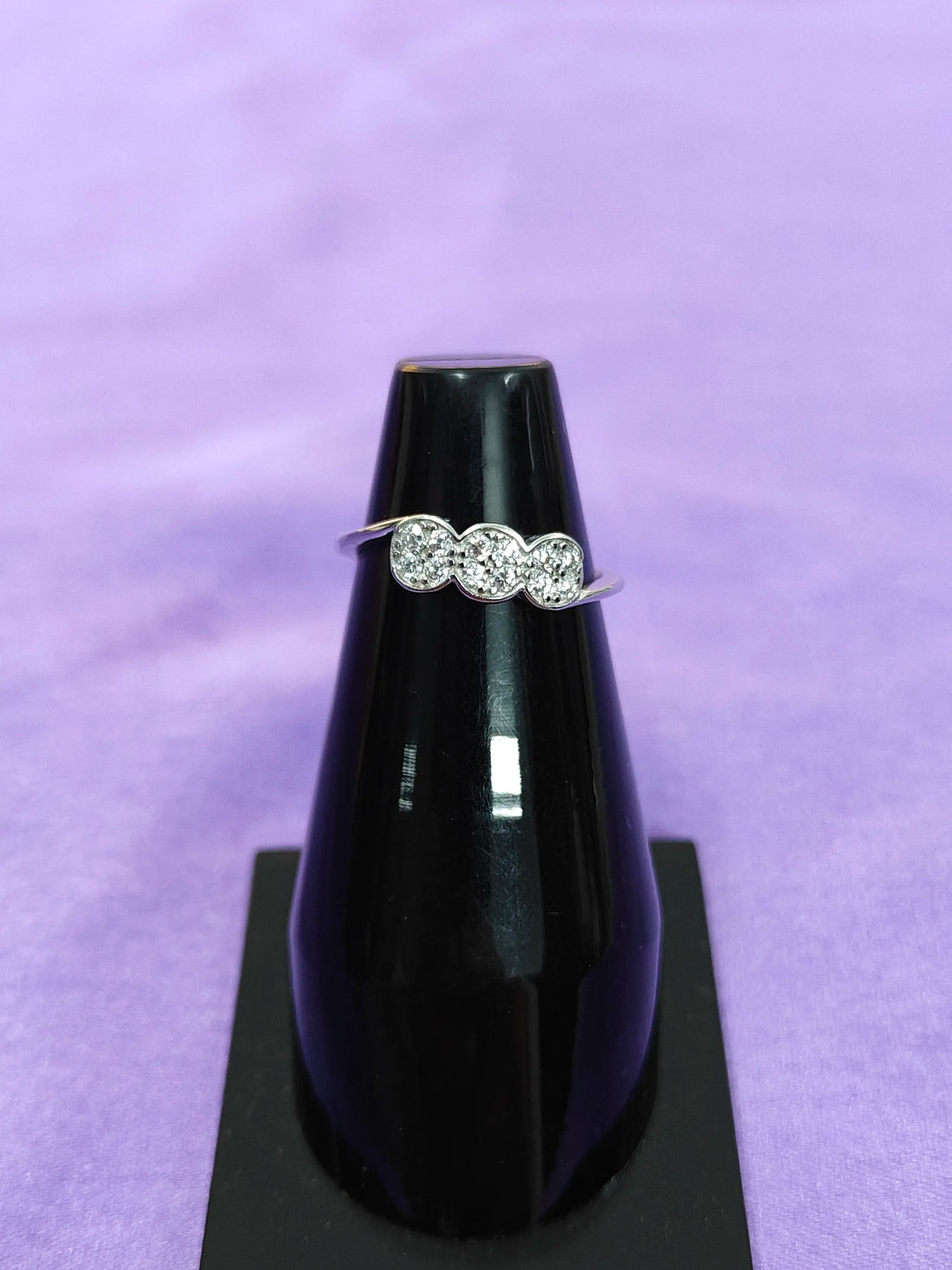 Diamond ring on a black stand against a purple background