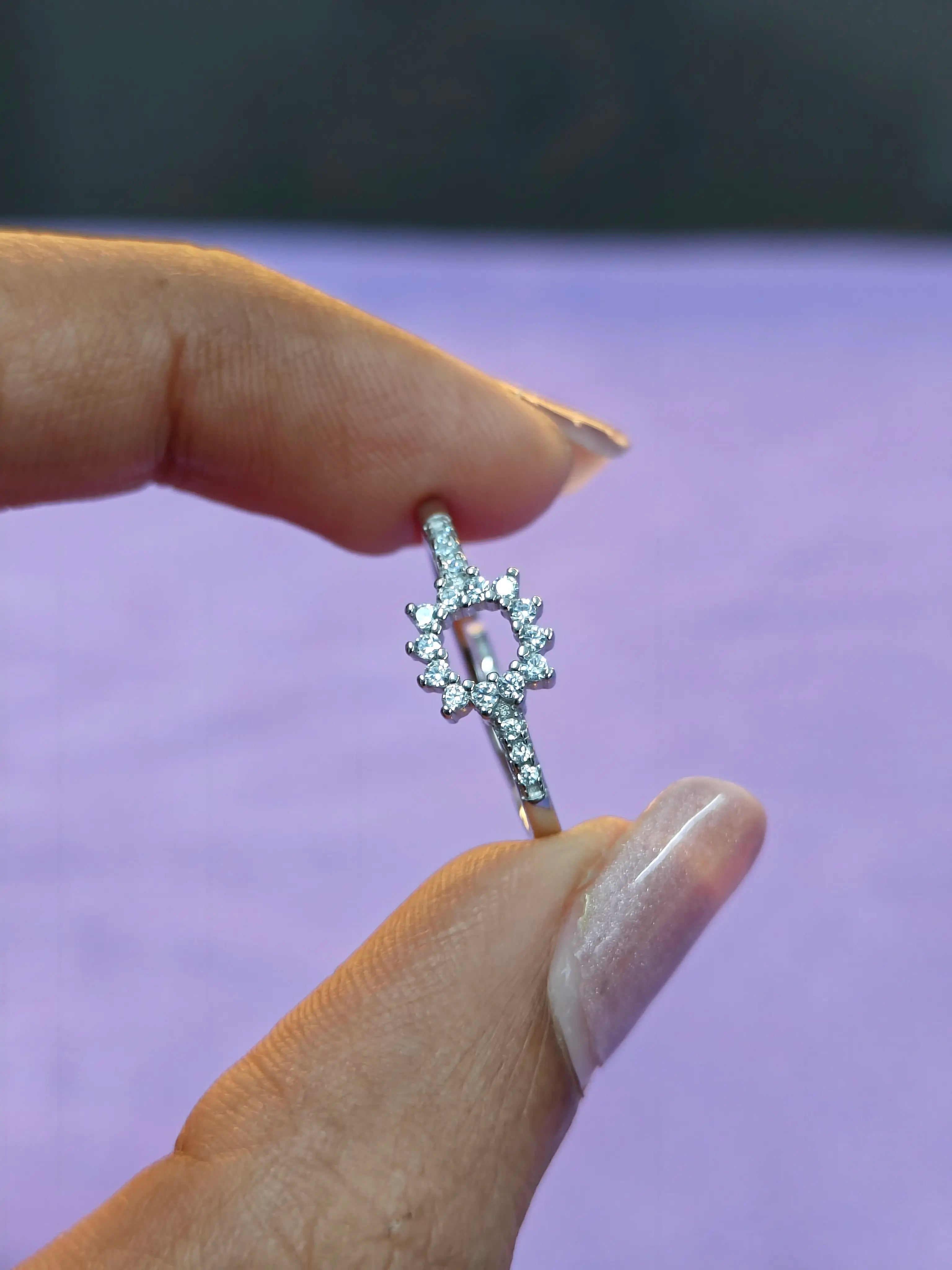 Silver bow-shaped earring held between fingers against a purple background